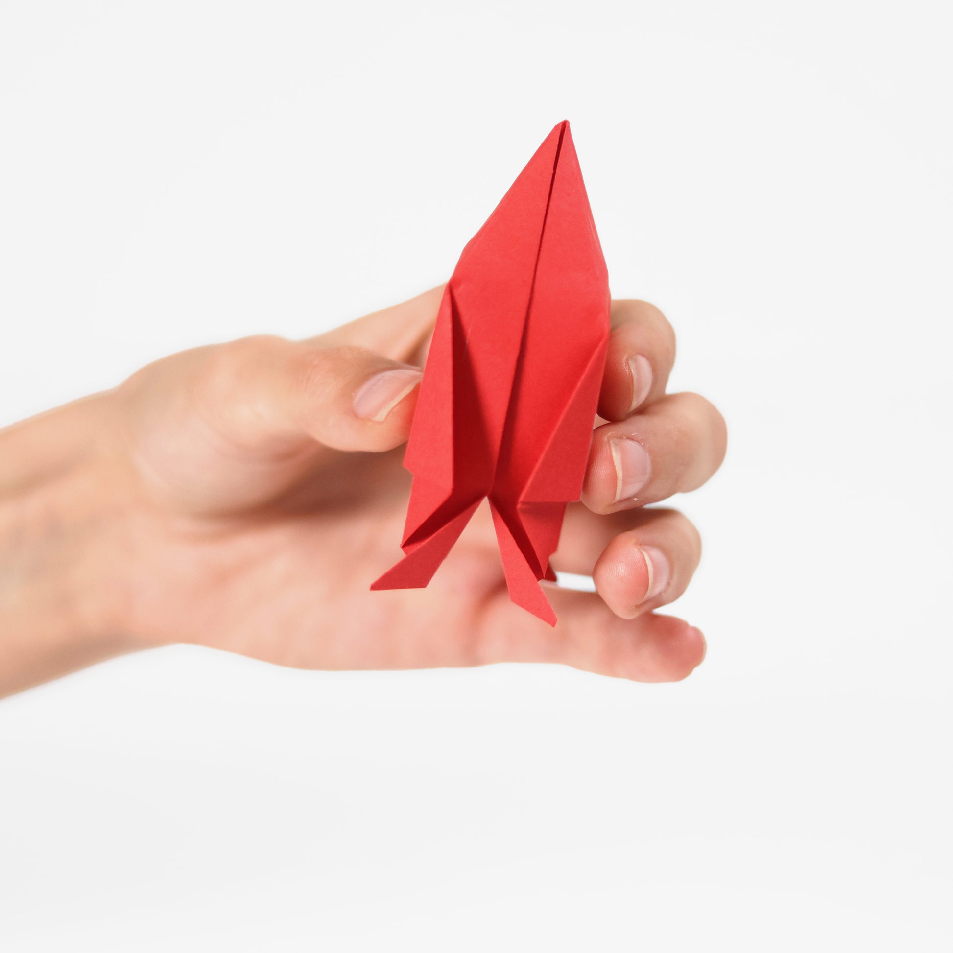 Red paper rocket from Pikkii Flying Paper Rockets kit - DIY paper rocket craft set in multi-color FSC-style printed sheets, includes materials for 20 foldable rockets in 3 shapes, blow launchers, 100+ stickers, and step-by-step instructions; lightweight fun craft kit for kids ages 6+.