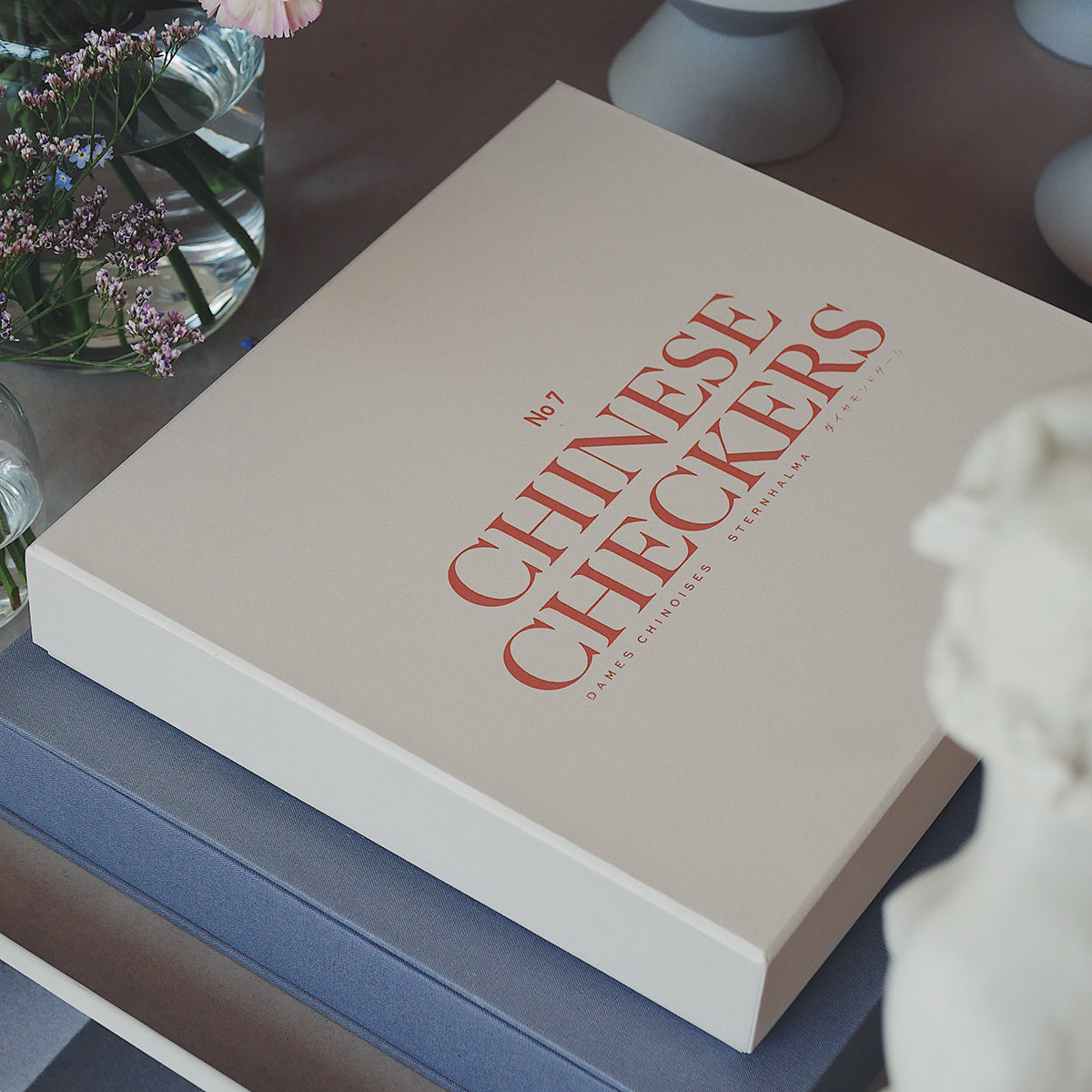 Printworks classic chinese checkers game beige box with peach font on an angle on a coffee table with flowers 