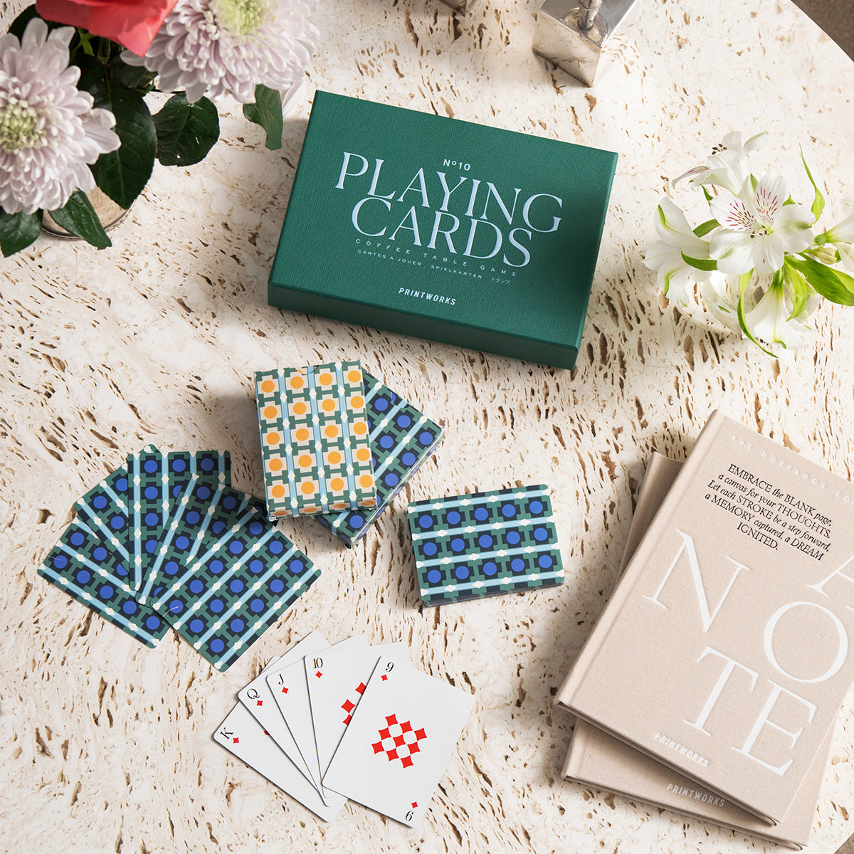 Showing playing cards on a table with the box from Printworks Classic Games double playing cards - twin deck set in modern stylish box, multi-color premium cardstock material with refined graphics, durable finish and elegant storage case.