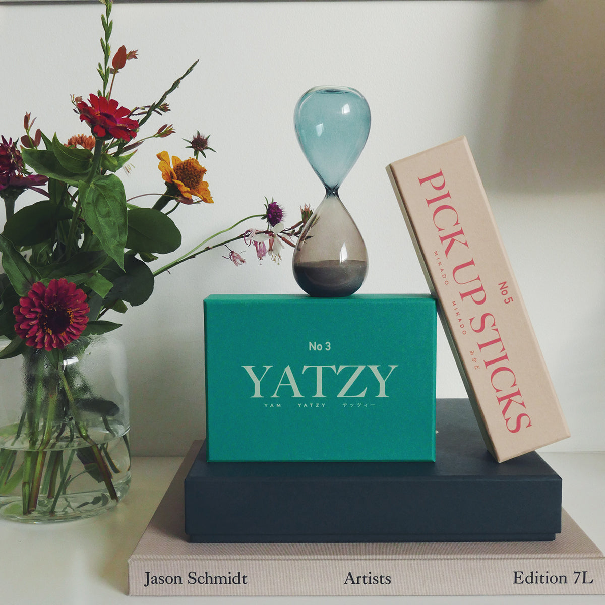 Printworks classic games yatzy aqua box with an hourglass on top, next to flowers an other games