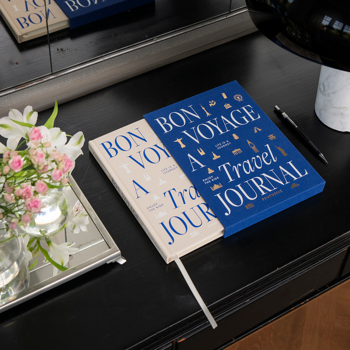 Printworks travel journal 'bon voyage' poking out of fabric bound cover on a black table with flowers