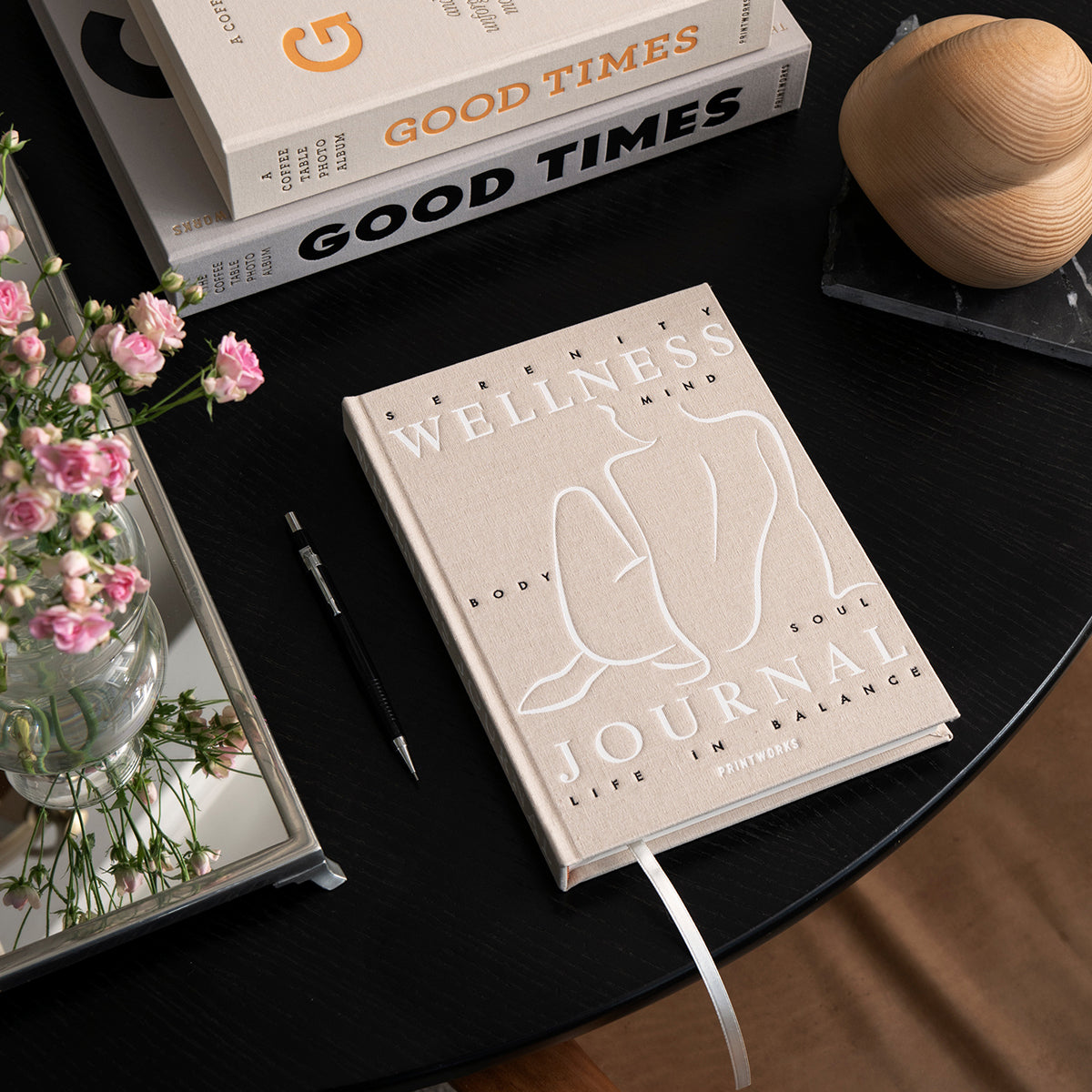 Printworks wellness journal laying flat on a black round gtalbe with books and wooden scuplture