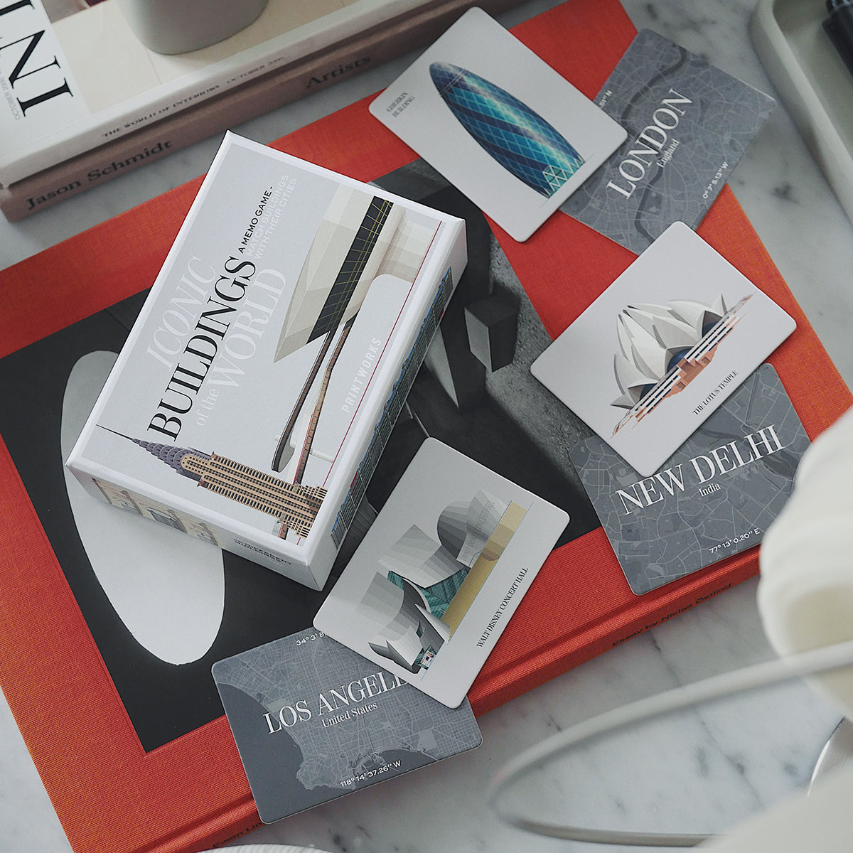 Printworks famous buildings memory game box and loose cards on red book on white marble table 