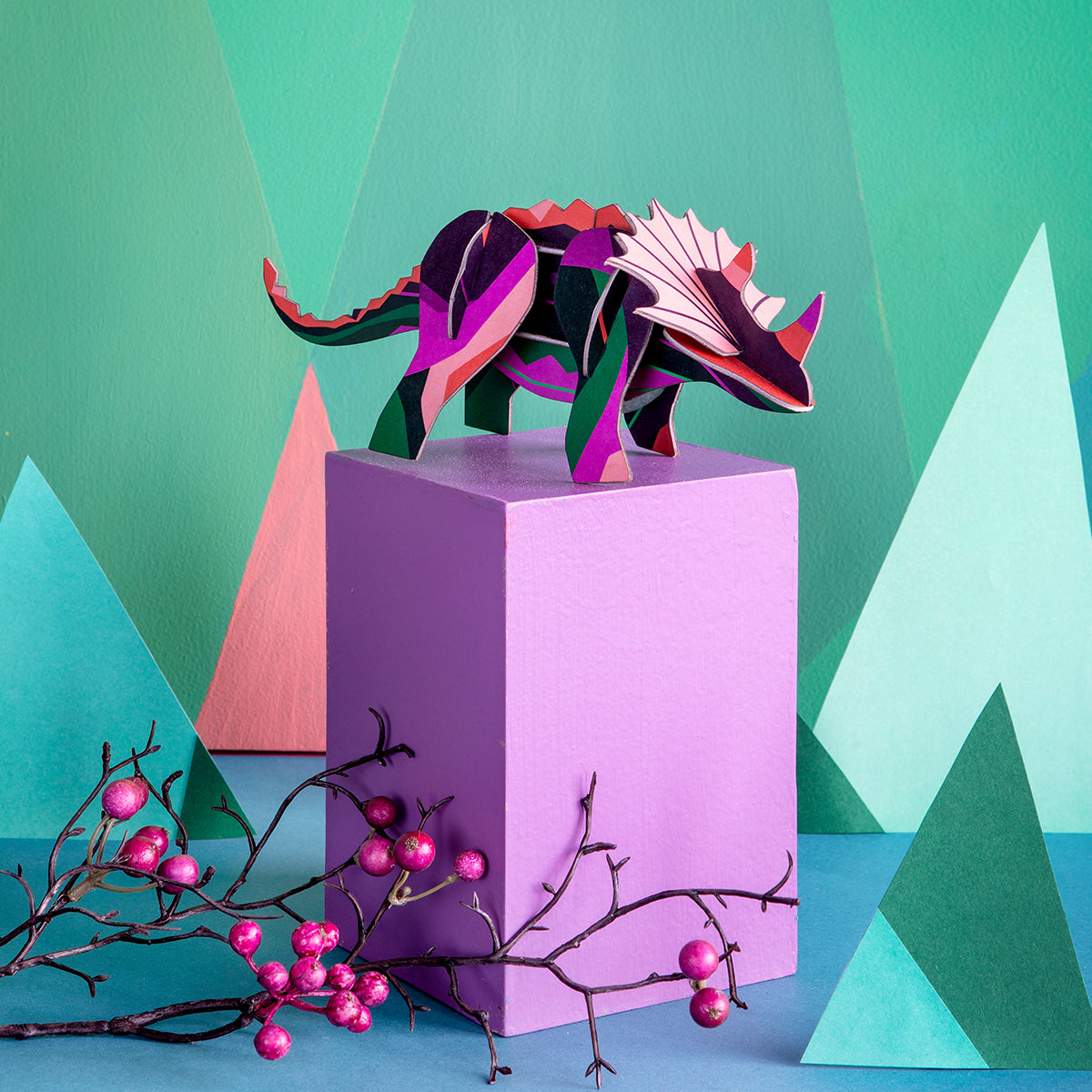Studio Roof B6 creative play card triceratops standing on top of a pink box with pink berries in the foreground and green background
