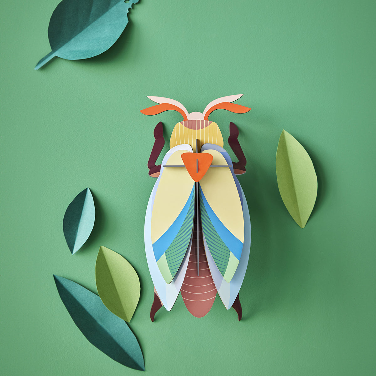 Studio Roof A4 lunar jewel beetle wall art hanging on a green background with green paper leaves