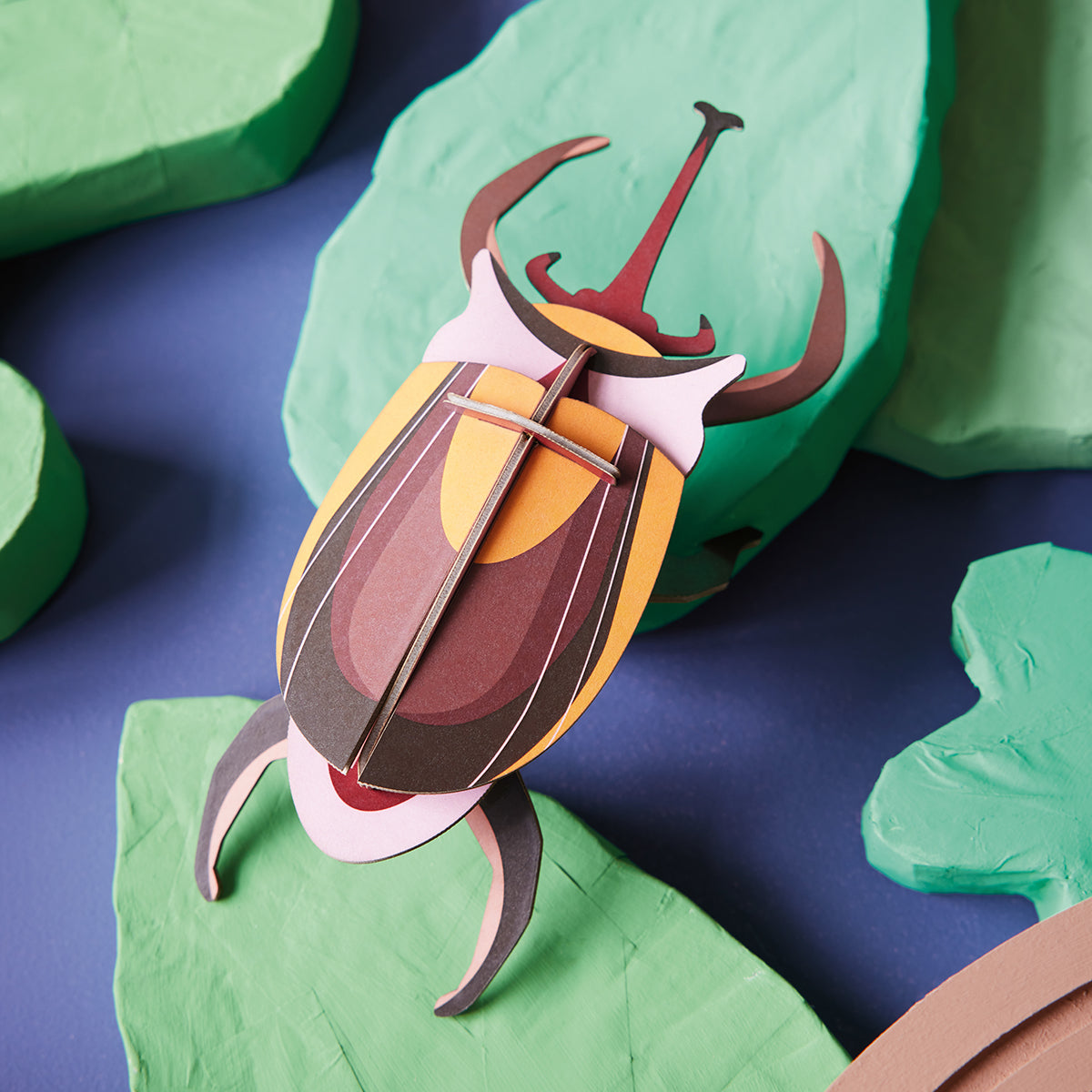 Close up of Studio Roof B7 elephant beetle wall art climbing on green leaves on purple background 