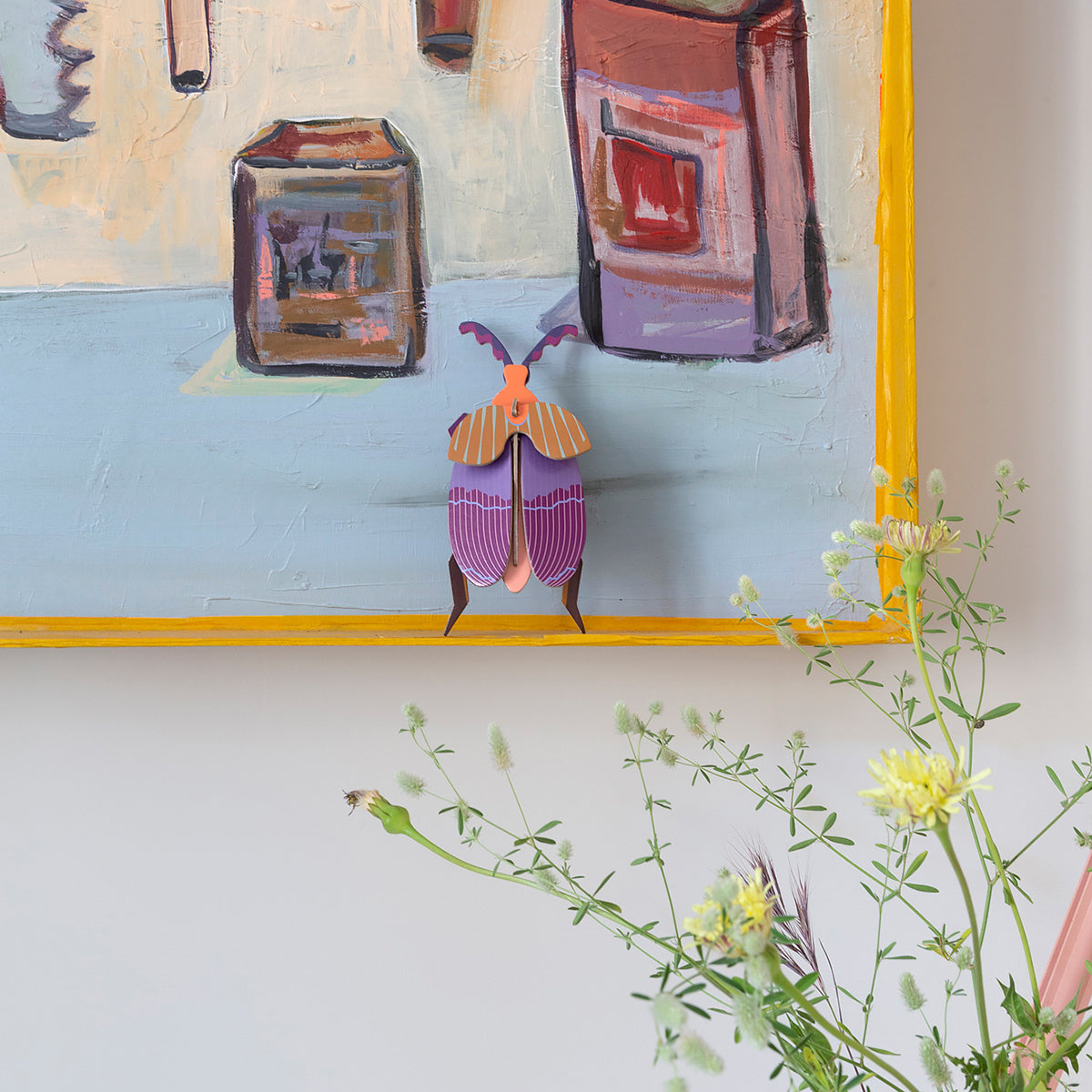 Studio Roof B7 queen beetle wall art on the corner of painting with yellow frame in front of yellow flowers