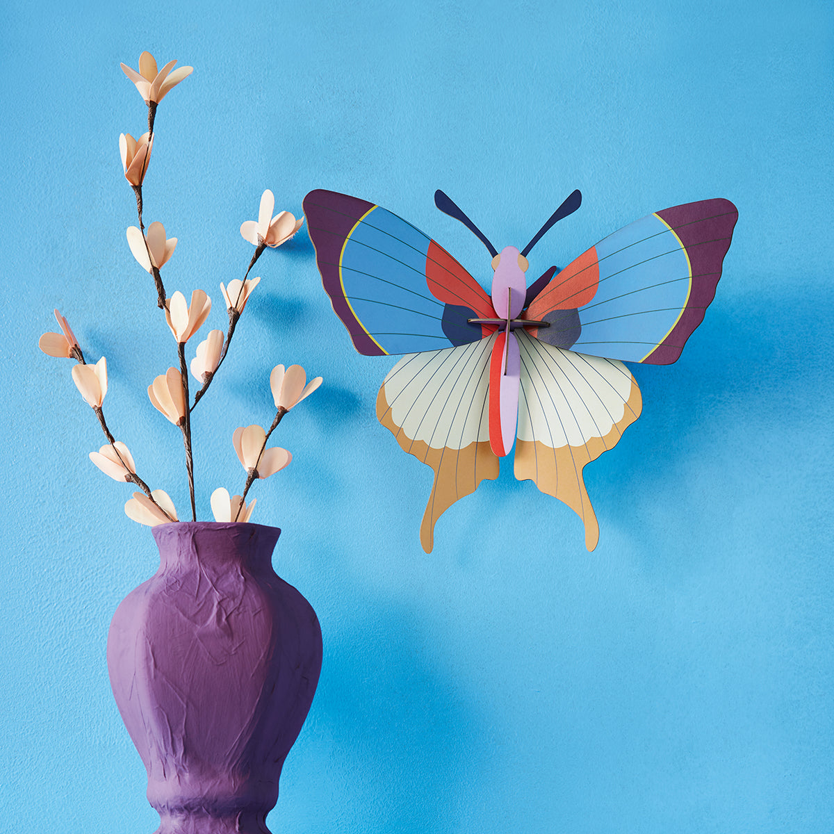 Studio Roof A4 plum fringe butterfly wall art on blue wall next to purple vase with white flowers