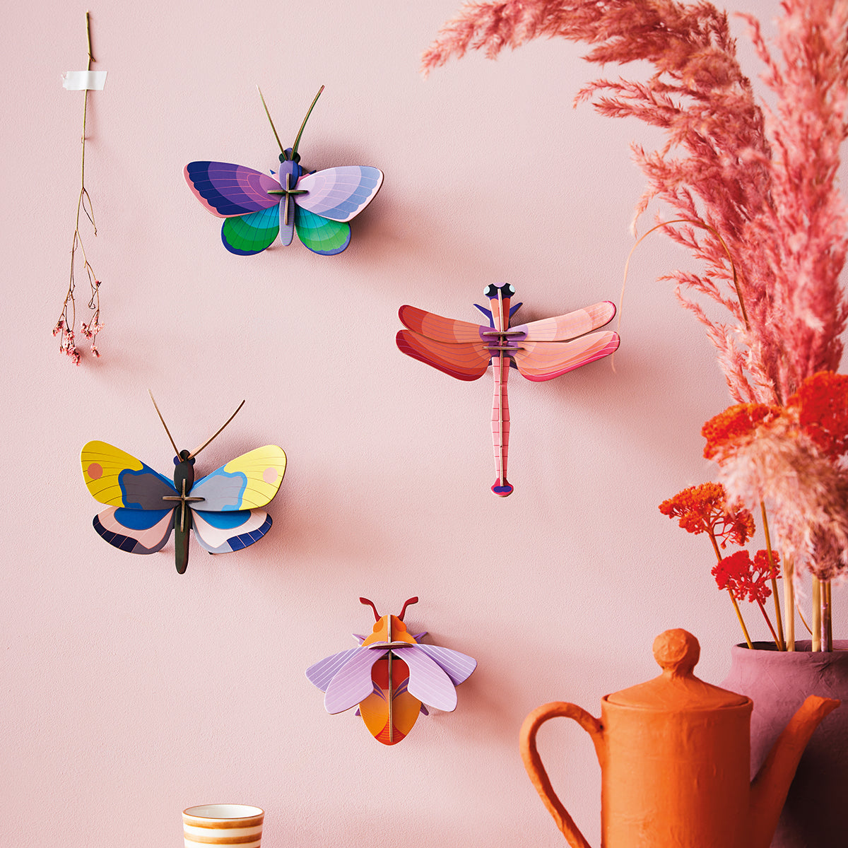 Studio Roof B7 blue copper butterfly wall art mounted on pale pink wall next to other butterflies next to pink vase with pink fronds