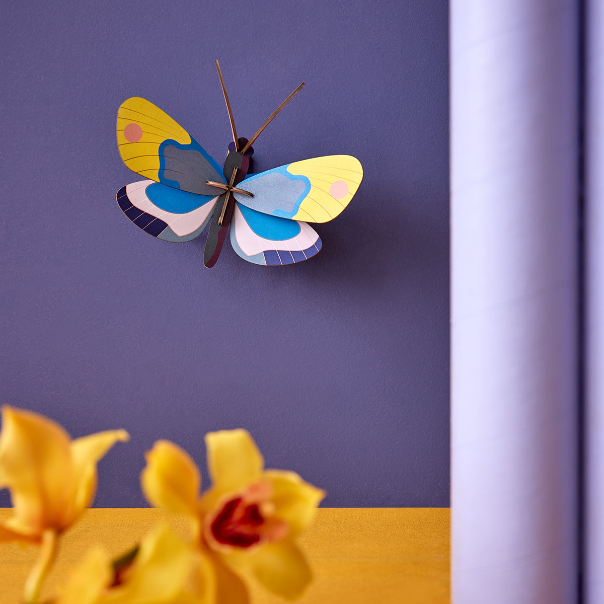Studio Roof B7 yellow monarch butterfly wall art on deep purple wall with yellow orchids in the foreground and pale purple pole