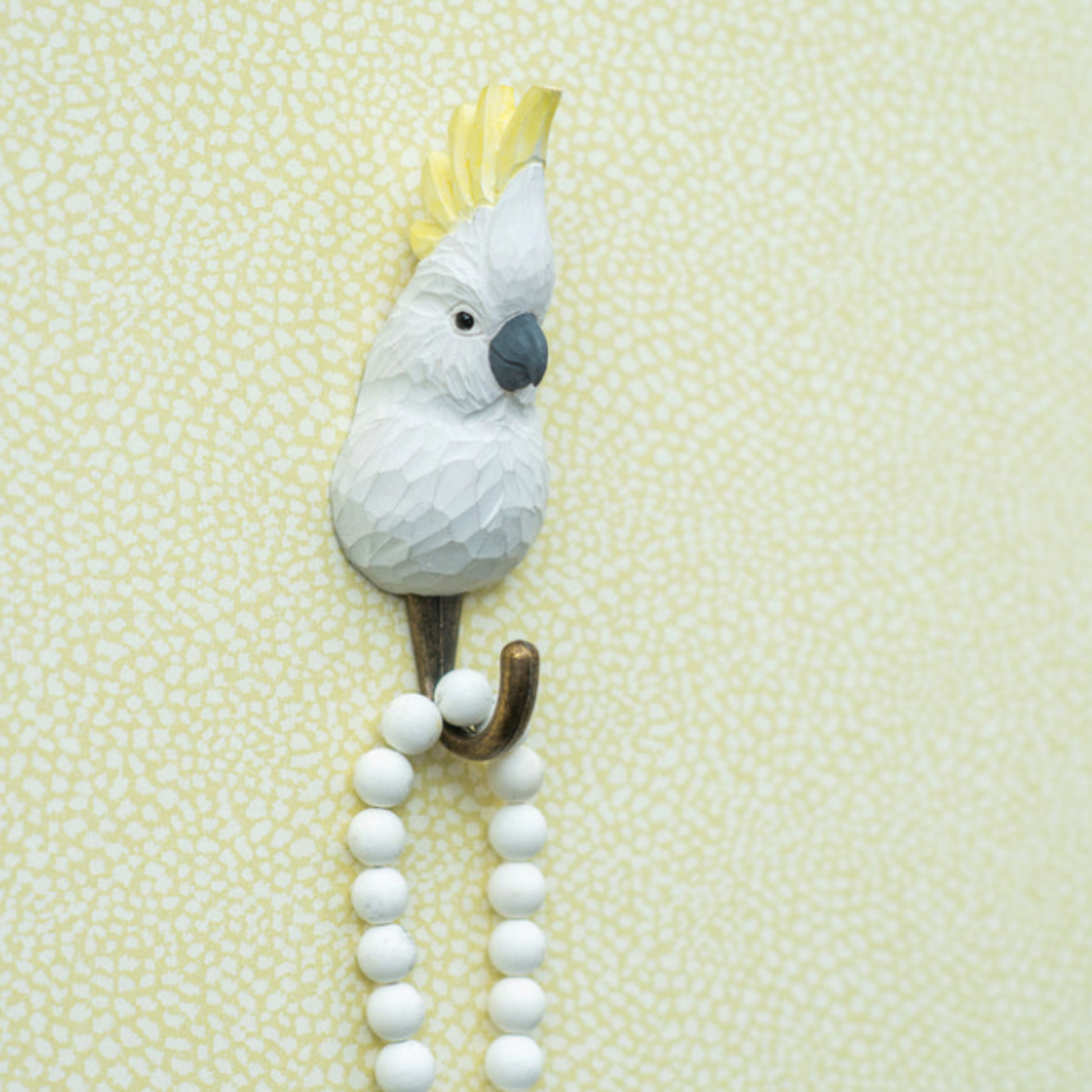 Close up of Wildlife Garden Wall Hook Sulphur Crested Cockatoo on wall with beads hanging on wall 