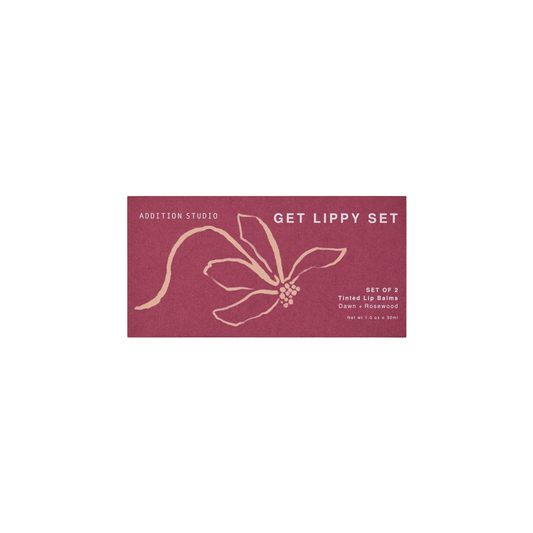 The red box of the Addition Studio Get Lippy Set for Dawn and Rosewood tinted lip balms made with camellia seed oil for hydration, nourishment, and improved skin elasticity, with arnica flower extract.