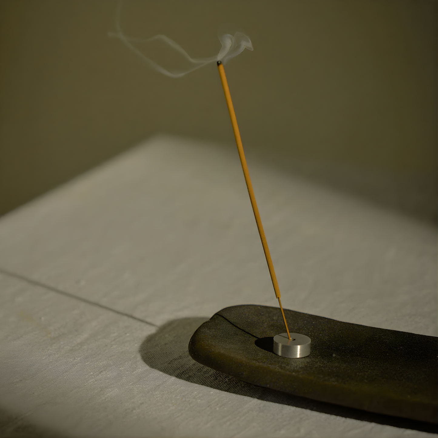 Shown an incense being lit on a holder, both from the Addition Studio Incense Set Cedarwood, Sage & Geranium (with Holder): a 15 incense stick with holder in an aluminum tube. A blend of cedar, geranium, lavandin, clary sage, Roman chamomile, and spearmint essential oils.