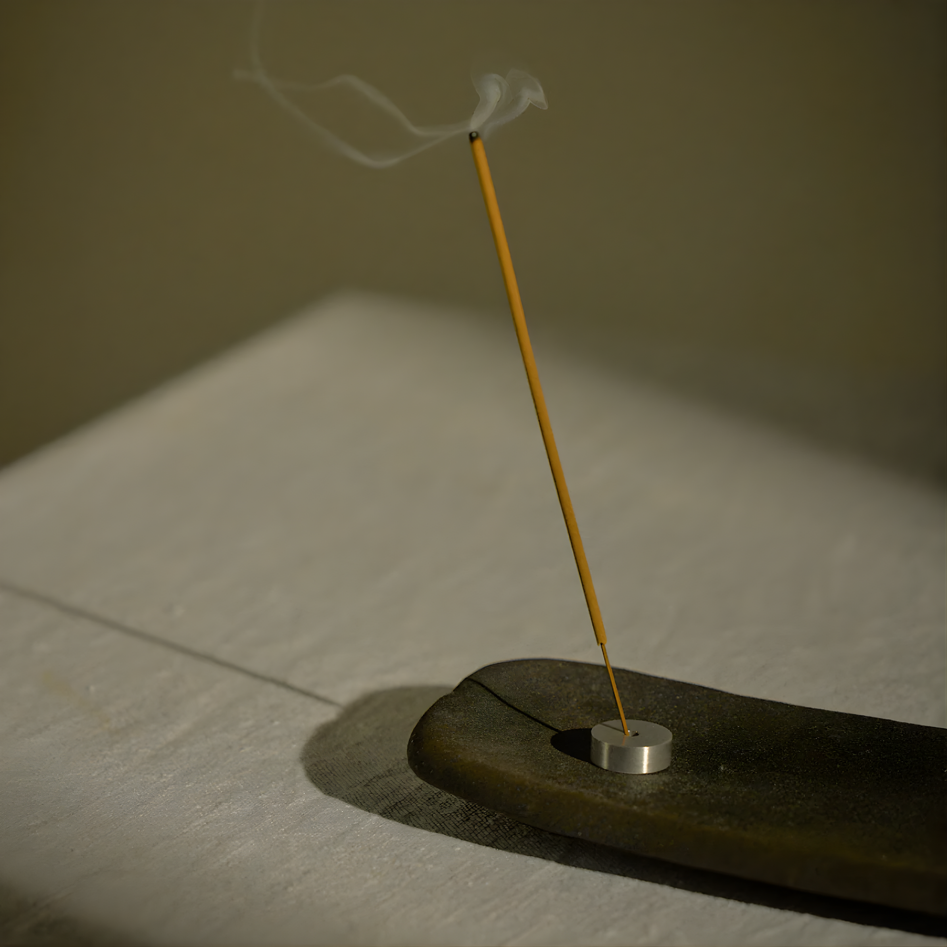 Shown an incense being lit on a holder, both from the Addition Studio Incense Set Cedarwood, Sage & Geranium (with Holder): a 15 incense stick with holder in an aluminum tube. A blend of cedar, geranium, lavandin, clary sage, Roman chamomile, and spearmint essential oils.