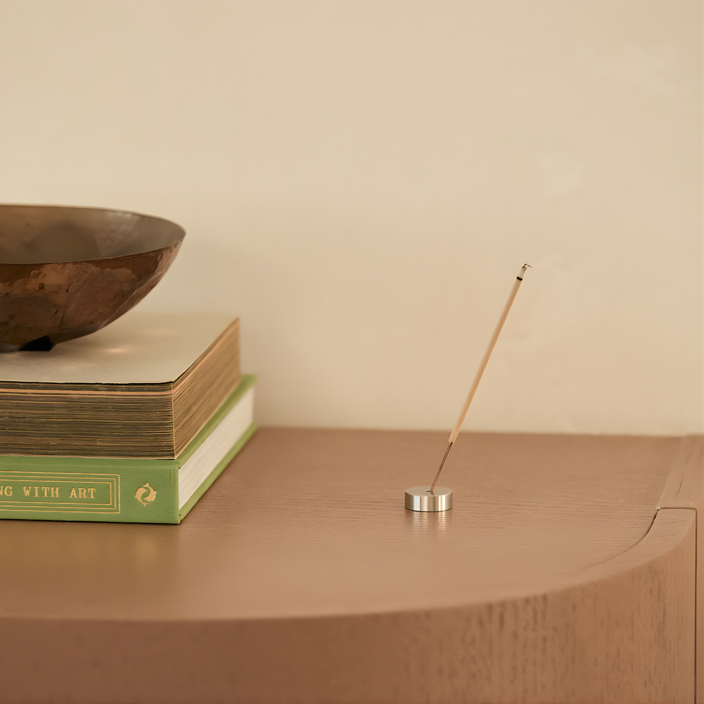 A lit incense on a holder on a wooden table from Addition Studio Incense Set Mandarin, Lime & Basil (with Holder): 15 incense sticks with holder in an aluminum tube. A blend of mandarin, sandalwood, lime, basil, and aniseed essential oils.