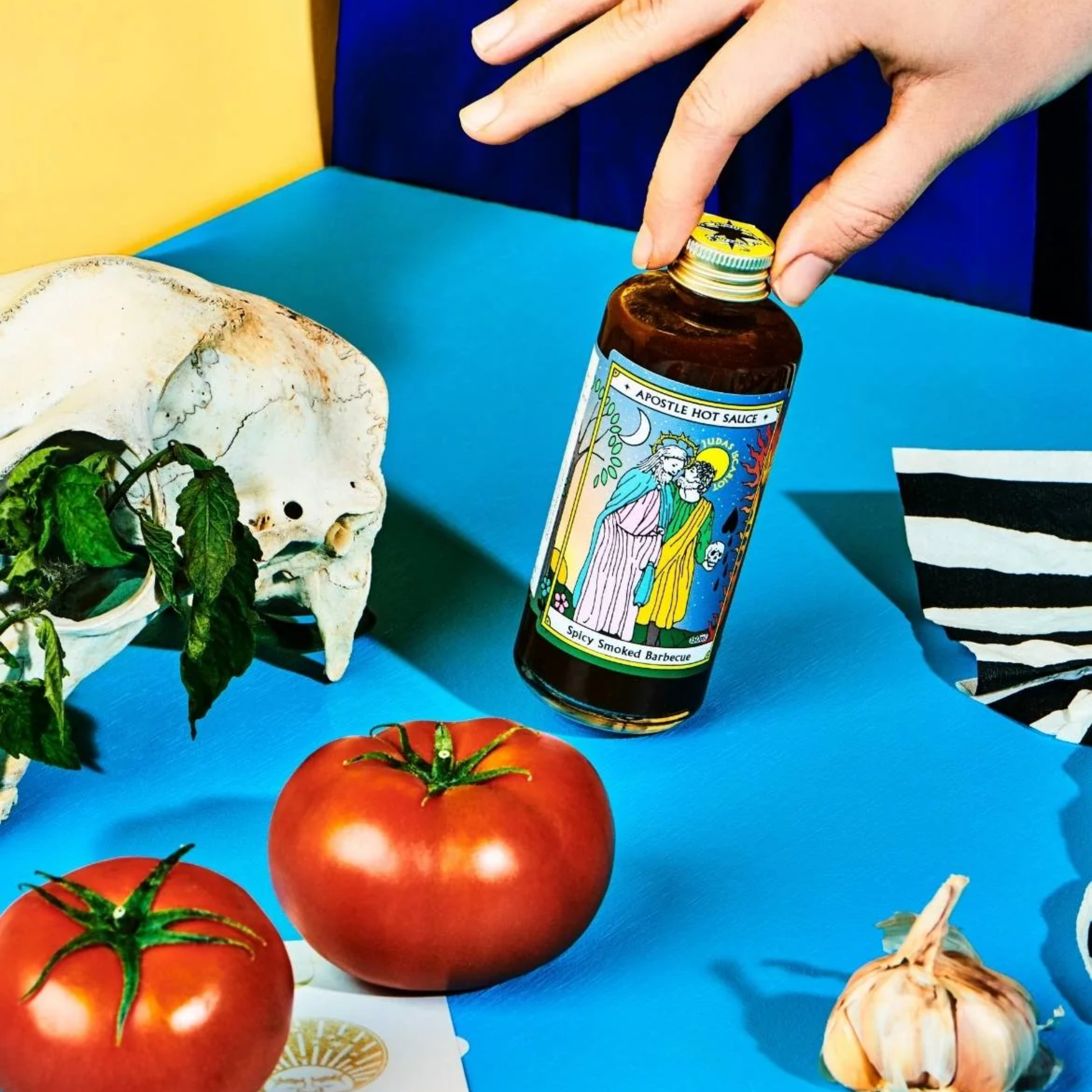 On a table the bottle of the Apostle Judas Iscariot Spicy Smoked Barbecue 150ml with inspiration from Louisiana barbecue, british brown sauces and carribbean jerk flavours.