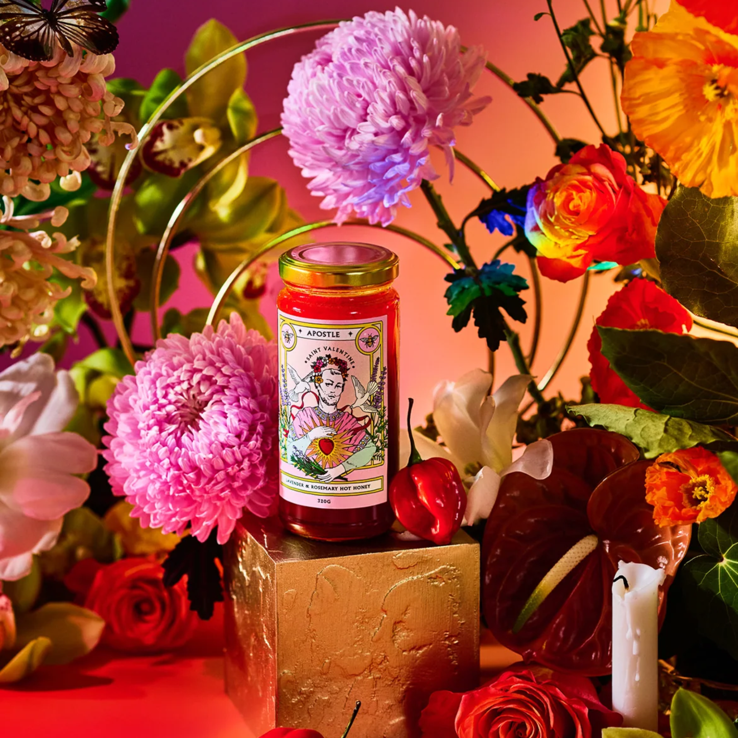On a cube surface with flowers around it, the bottle Apostle Saint Valentine Lavender & Rosemary Hot Honey 320g