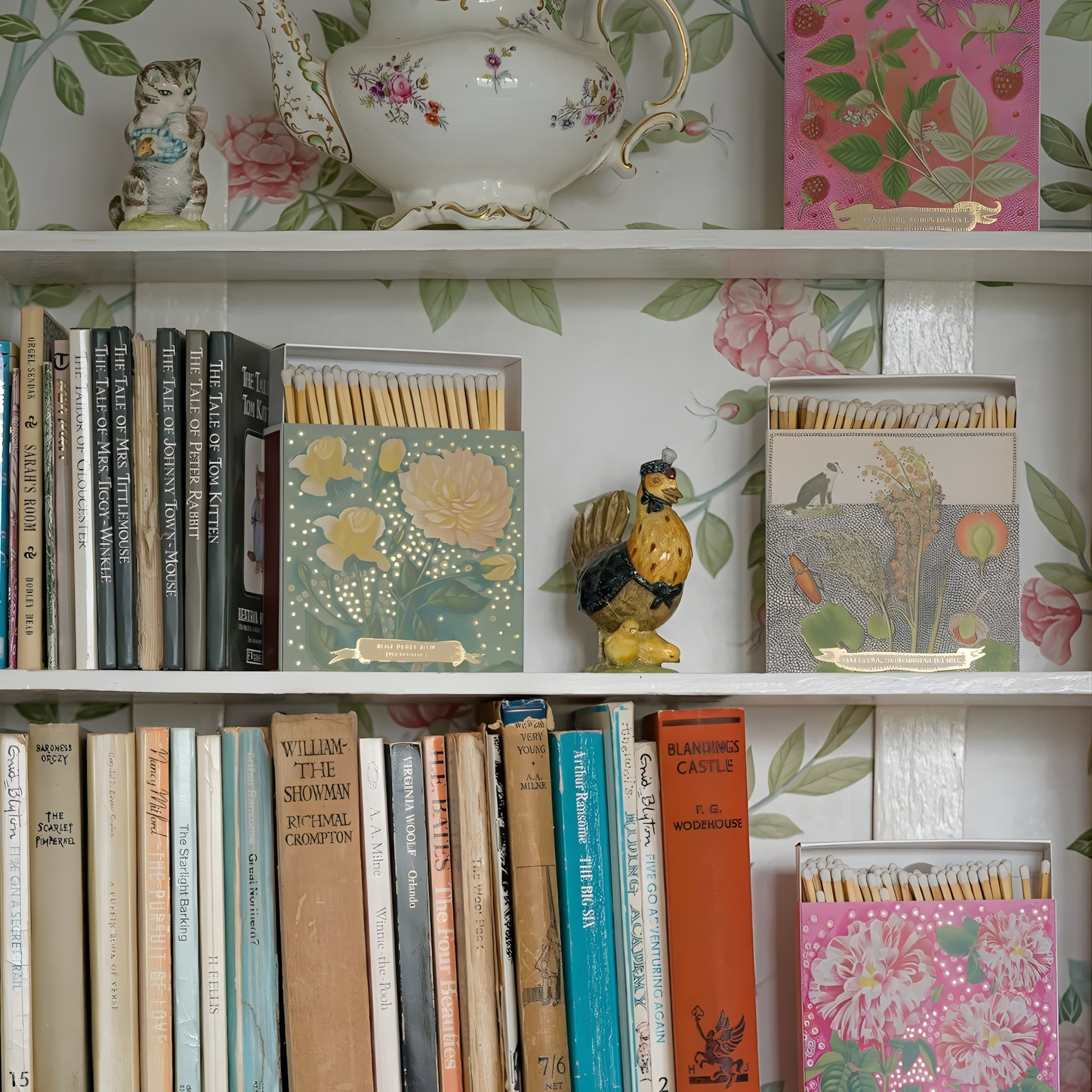 Seen with books and figurines on a shelf, the Archivist Luxury Matches Chien Botanical Drawing which features a green and orange floral illustration with a collie dog and gold foil detail by Florence Balducci. Contains 125 matches (100 mm, white tips). Litho printed in the UK with FSC-certified wood and wrapped in compostable cello-ideal for coffee tables, mantelpieces, or gifting.