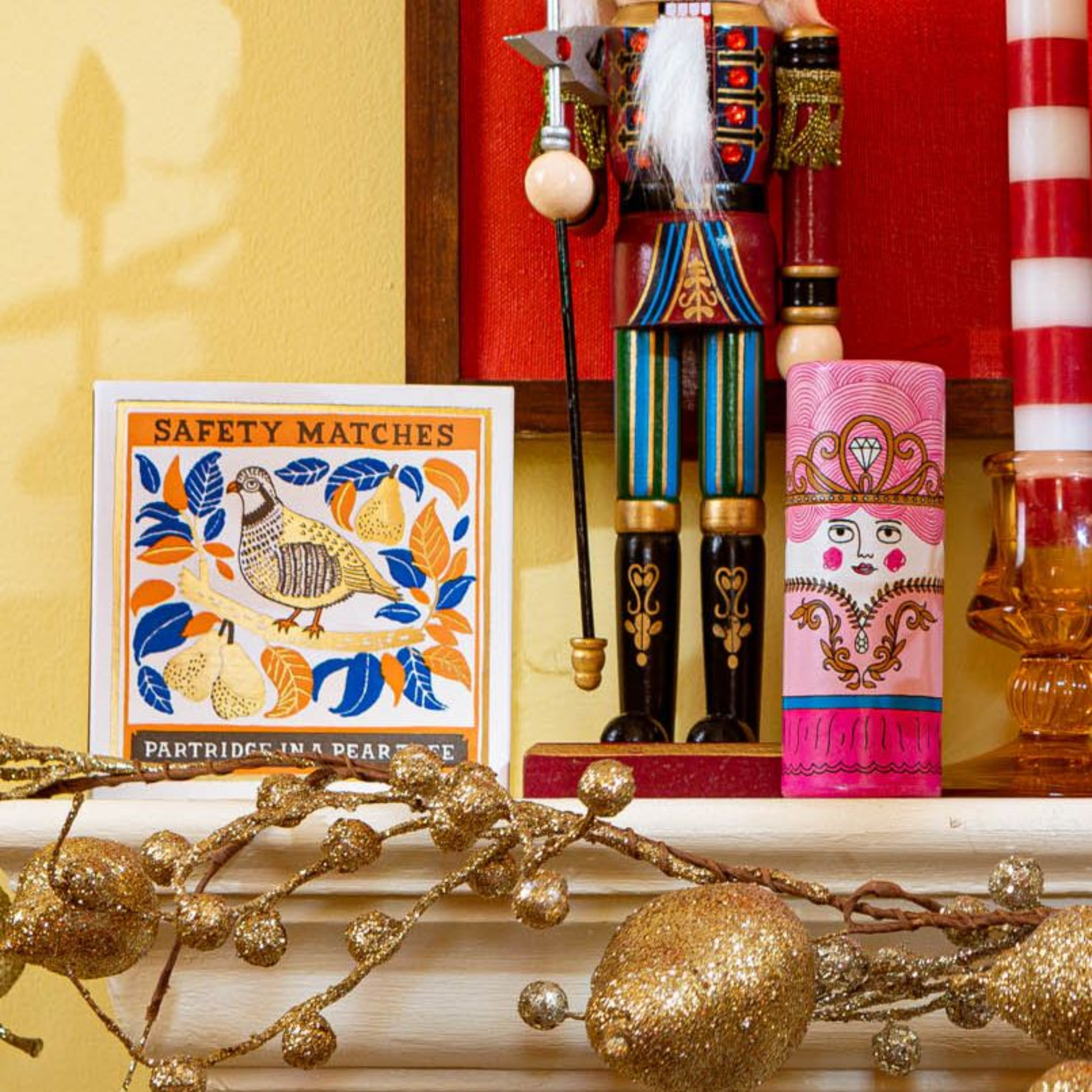 Front view with a decorative nutcraker showing size comparison with the Archivist Partridge in a Pear Tree Matches - Square Matchbox with Partridge and Pear Tree Design - Natural White-Tipped Matches - FSC Wood Material, UK Letterpress Print, Eco-Friendly Decorative Match Set