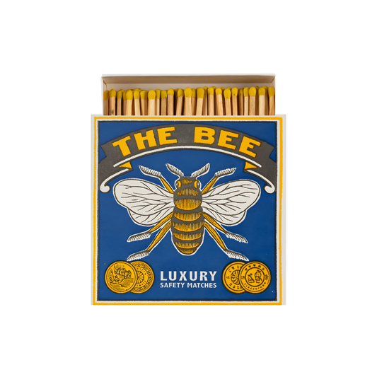 Front view and open Archivist Luxury Matches The Bee which features a bumblebee on a blue background with the words "The Bee, Luxury Safety Matches." Contains 125 matches (100 mm, yellow tips, white tray), letterpress printed in the UK with FSC-certified wood and wrapped in compostable cello-perfect for coffee tables, mantelpieces, or gifting.