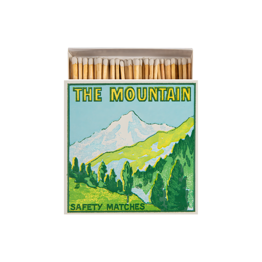 Front view and open Archivist Luxury Matches The Mountain: Features a snowy mountain range against a bright blue sky with the words "Safety Matches." Contains 125 matches (100 mm, yellow tips, white tray), letterpress printed in the UK with FSC-certified wood and wrapped in compostable cello-ideal for coffee tables, mantelpieces, or gifting.