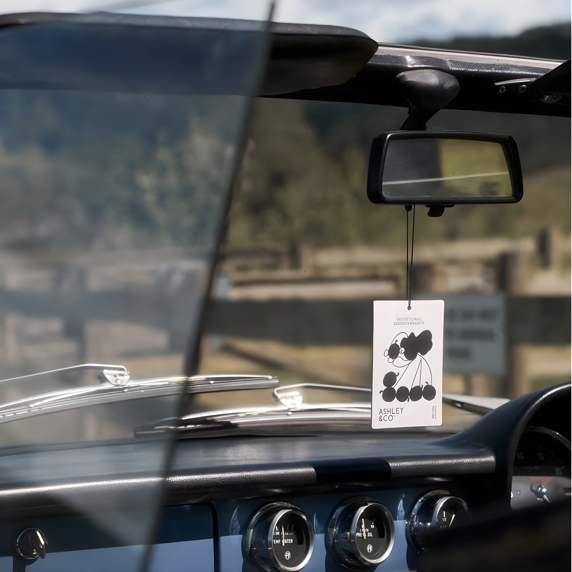 Front view of the Ashley & Co Carded Perfume Air Freshener Bonberry hung on the car rear view mirror.