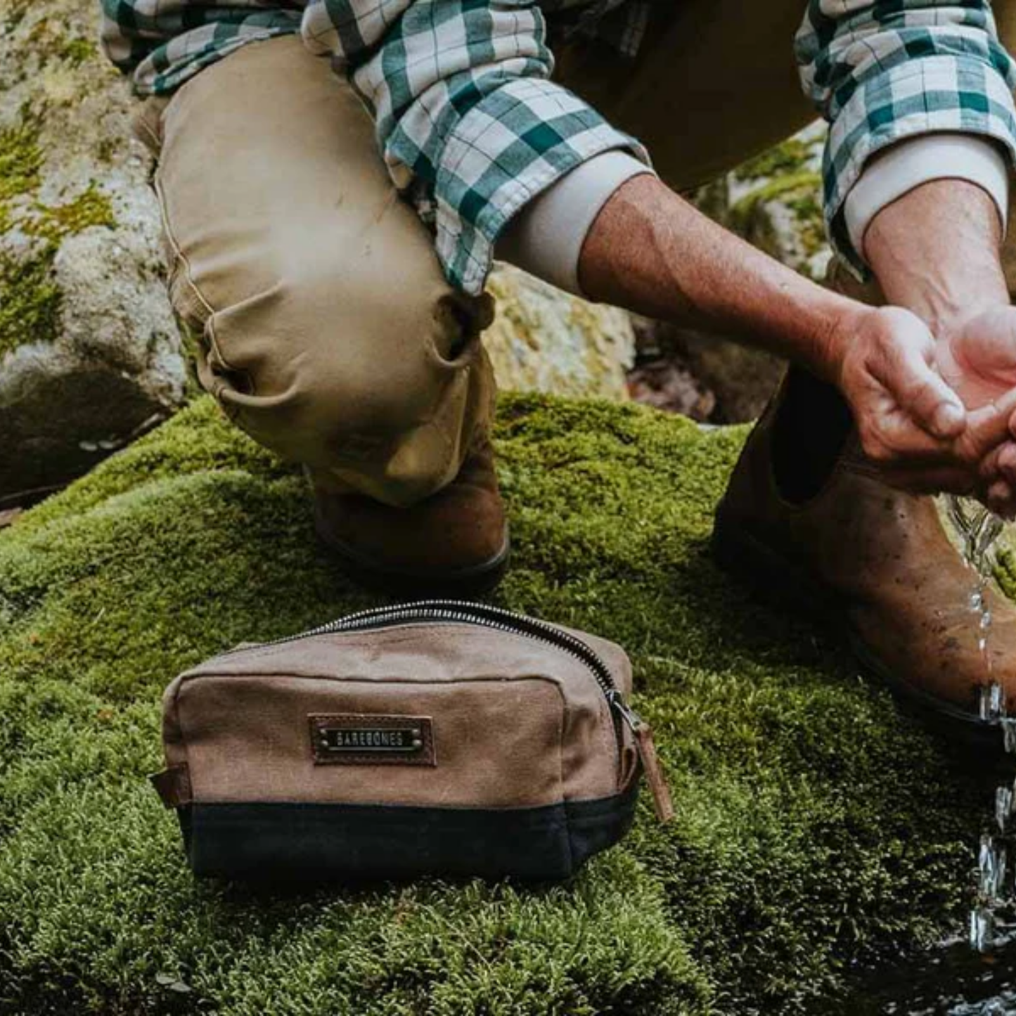 Man washing hands at river with Neelum drop kit on mossy rock
