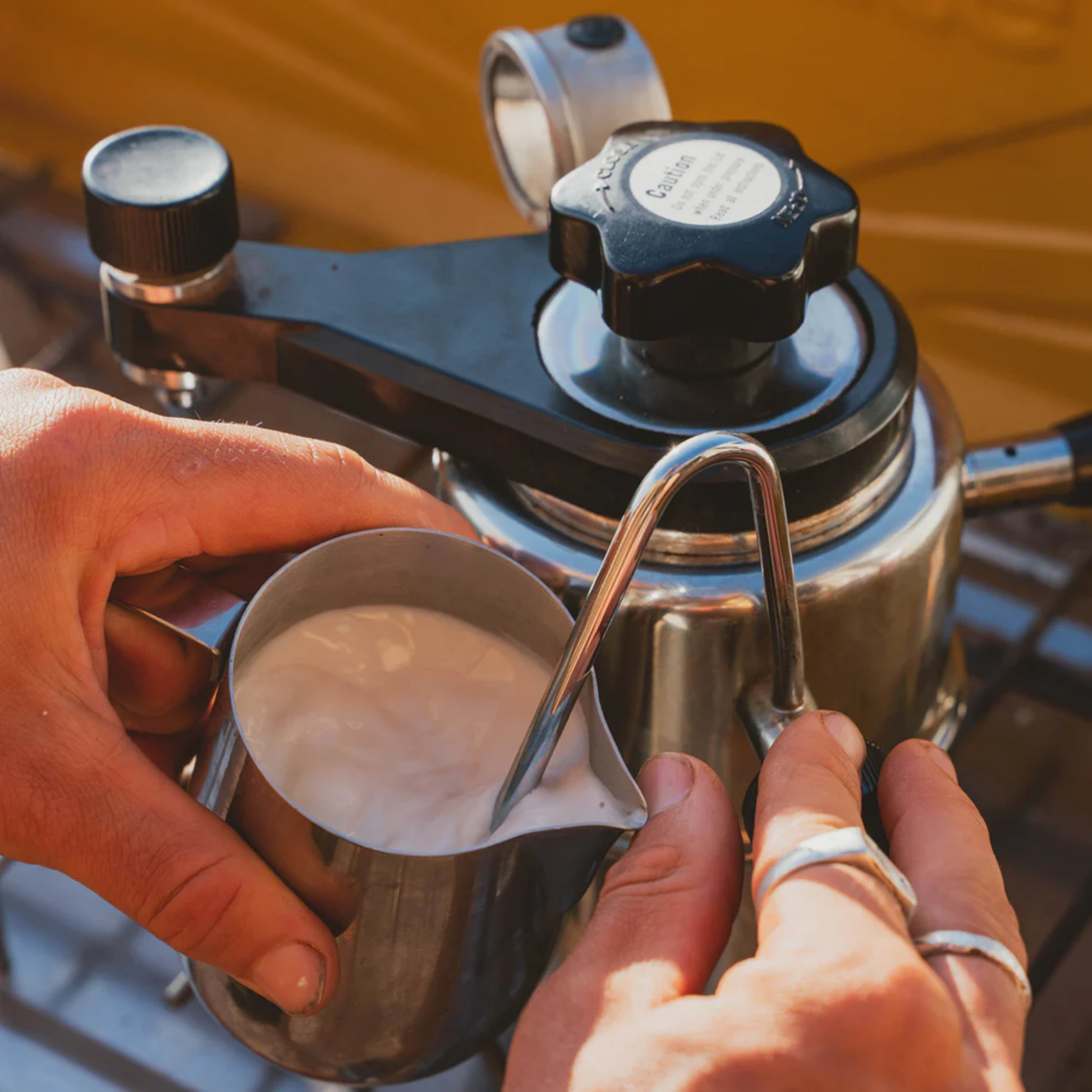 In use for frothing milk, Bellman Espresso & Steamer, silver stainless steel stovetop coffee maker, brews 3-9 cups of rich espresso with crema and velvety steamed milk, featuring a built-in pressure gauge for balanced extraction.
