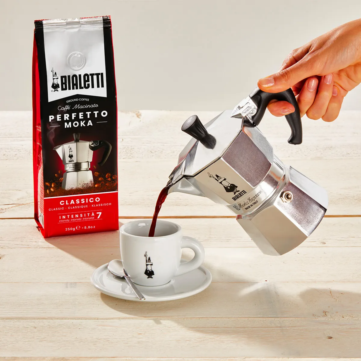 Bialetti Moka Express 1-cup stovetop coffee maker, shown pouring coffee, compact aluminum model with black handle and knob, designed to brew rich Italian espresso with a full-bodied aroma, Made in Italy.
