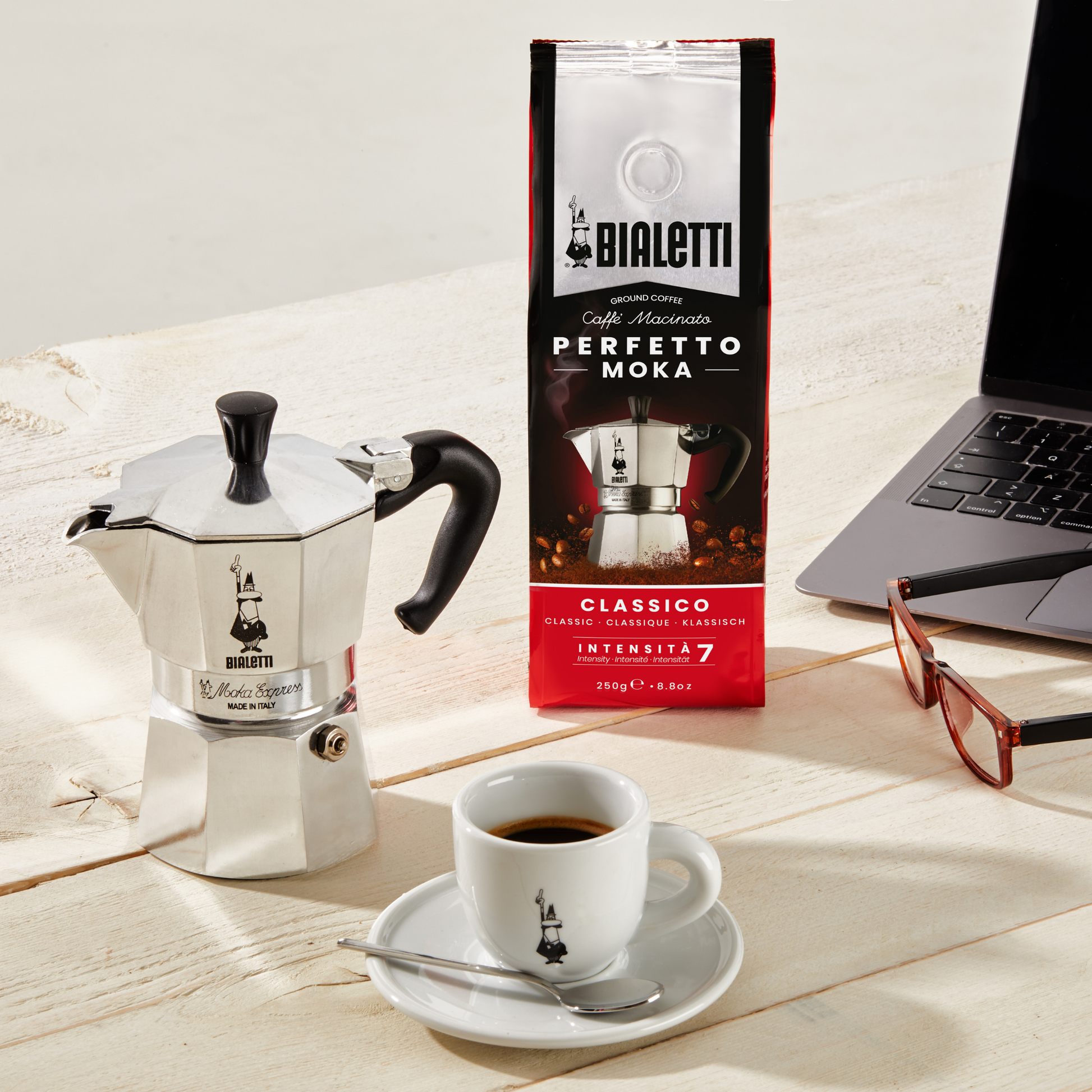 Bialetti Moka Express 2-cup stovetop coffee maker, shown with a cup of coffee, small aluminum model with black thermoplastic handle and knob, ideal for brewing up to two cups of authentic Italian espresso with rich crema.