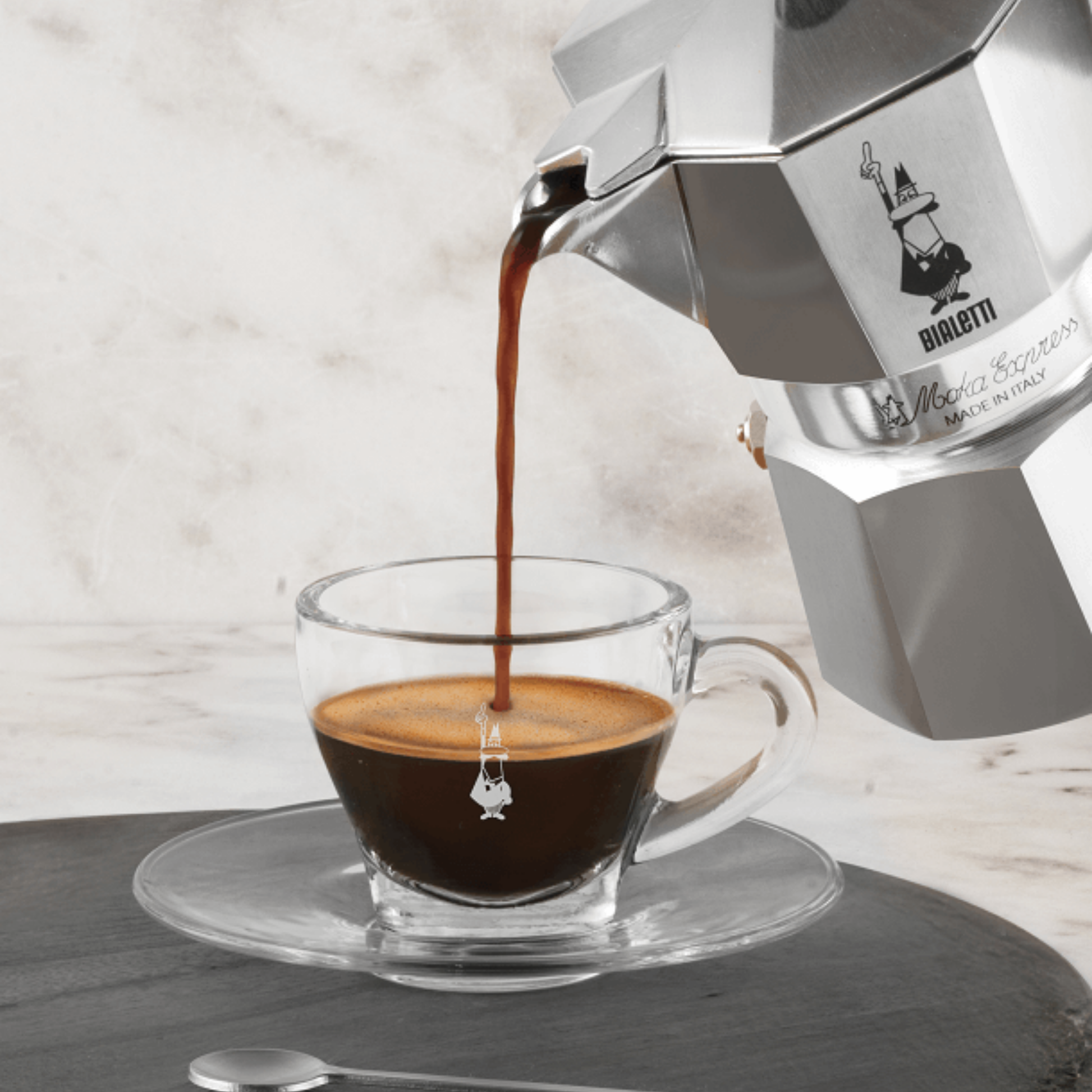 Bialetti Moka Express 4-cup stovetop espresso maker, shown pouring coffee made, aluminum body with black handle and knob, classic octagonal design that produces smooth, aromatic espresso for four servings.
