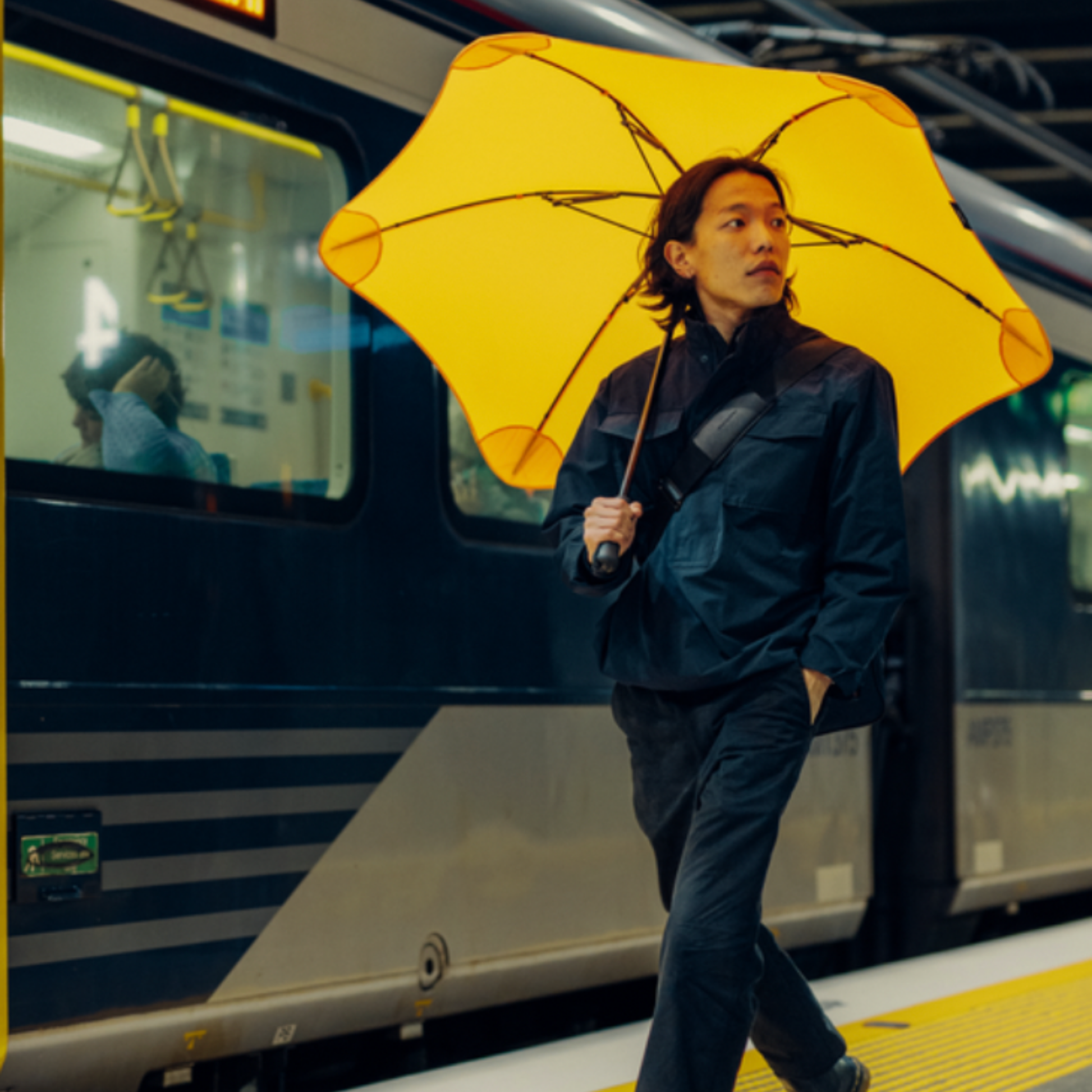 Man by train holding Blunt classic unbrella citrus yellow over shoulder