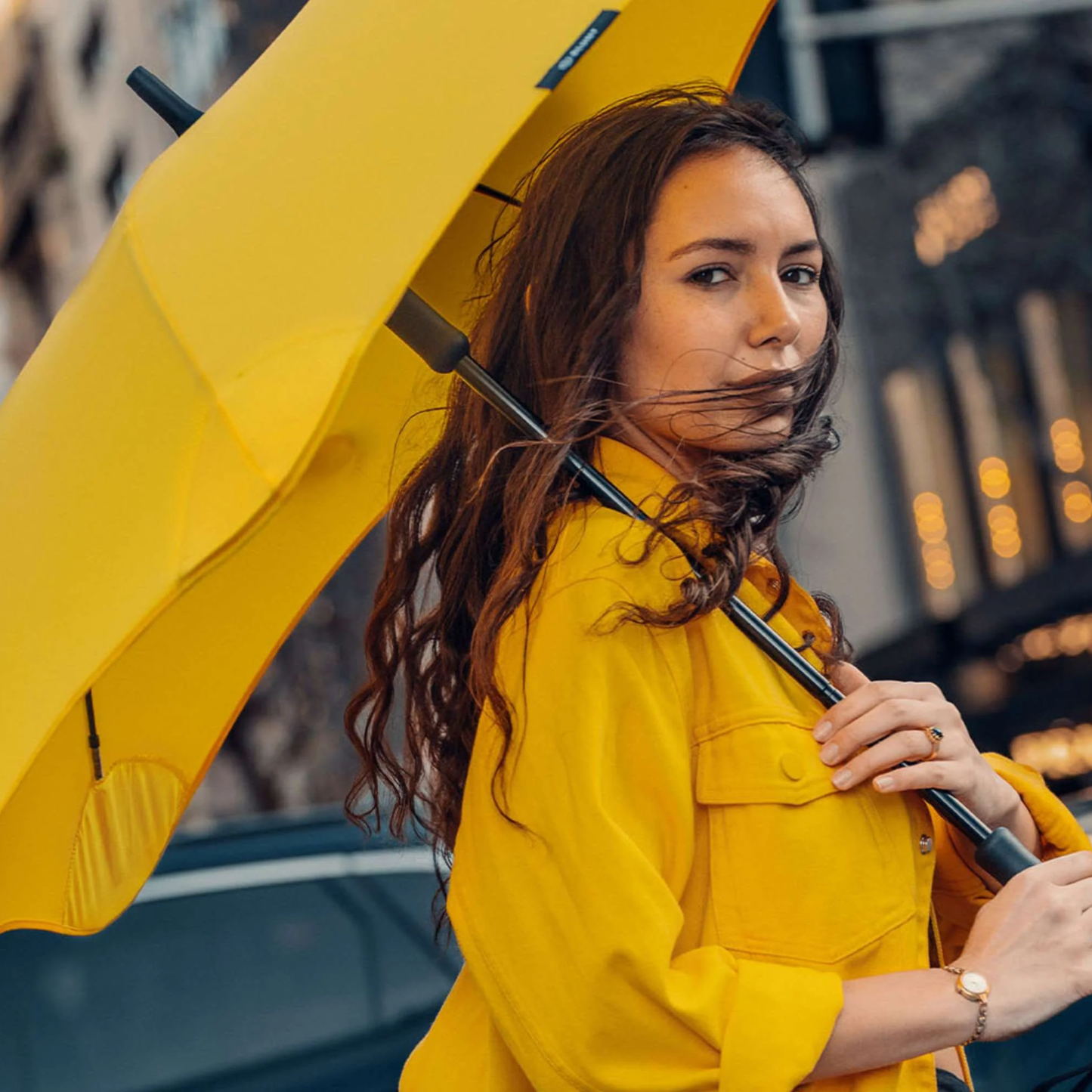 Side view of a woman holding the open Blunt Umbrella Classic Citrus Yellow in original full length that consist of the detachable UV fabric canopy, sturdy frame, shaft and handle. Ideal protection from heavy downpour or any weather.