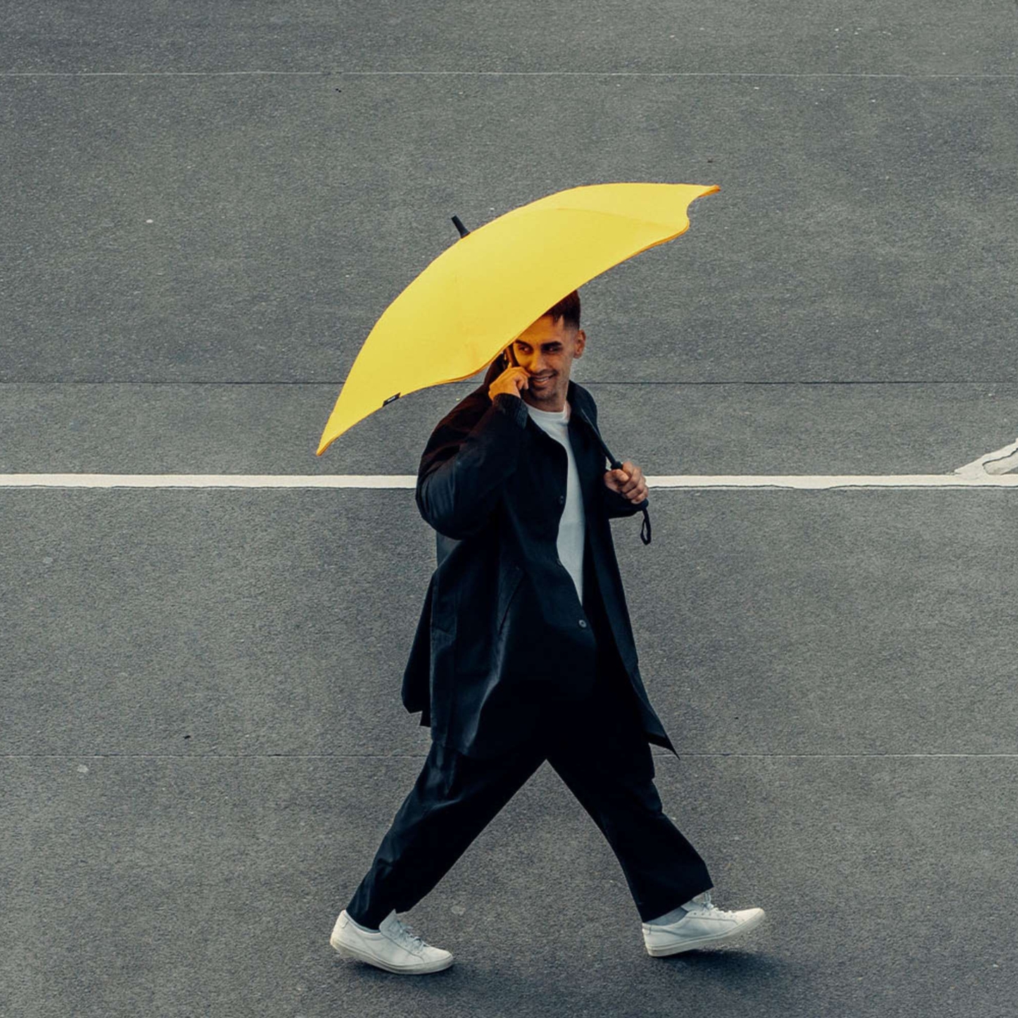 A man crossing the street while using the Blunt Umbrella Classic Citrus Yellow in original full length that consist of the detachable UV fabric canopy, sturdy frame, shaft and handle. Ideal protection from heavy downpour or any weather.