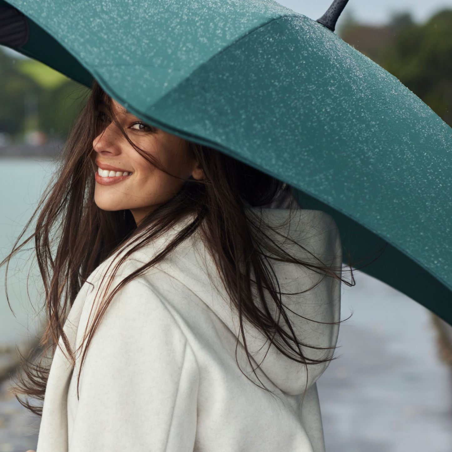 Woman simling holding Blunt forest green umbrella with raindrops on open umbrella 