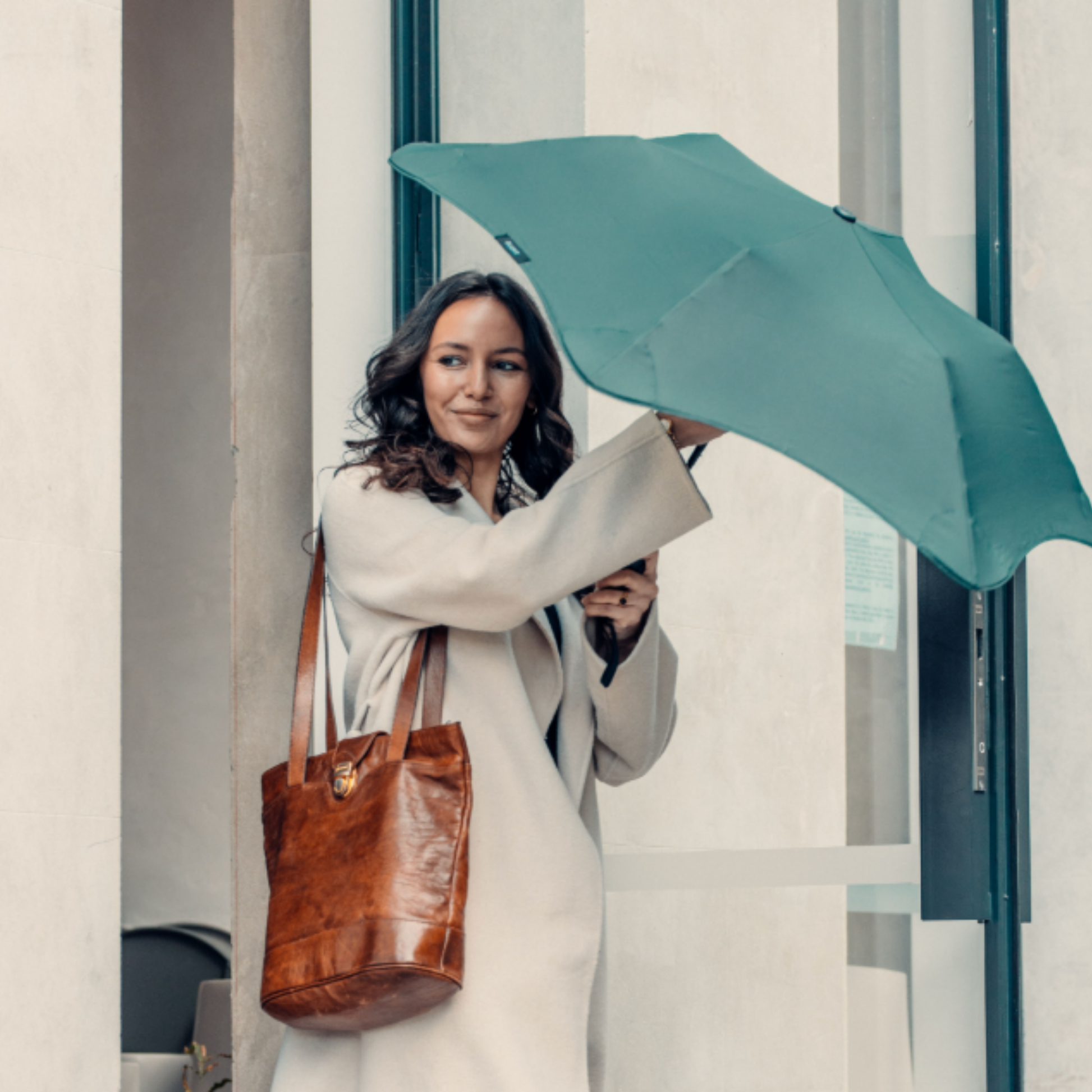 Woman leaving building erecting blunt forest green metro umbrella over head 