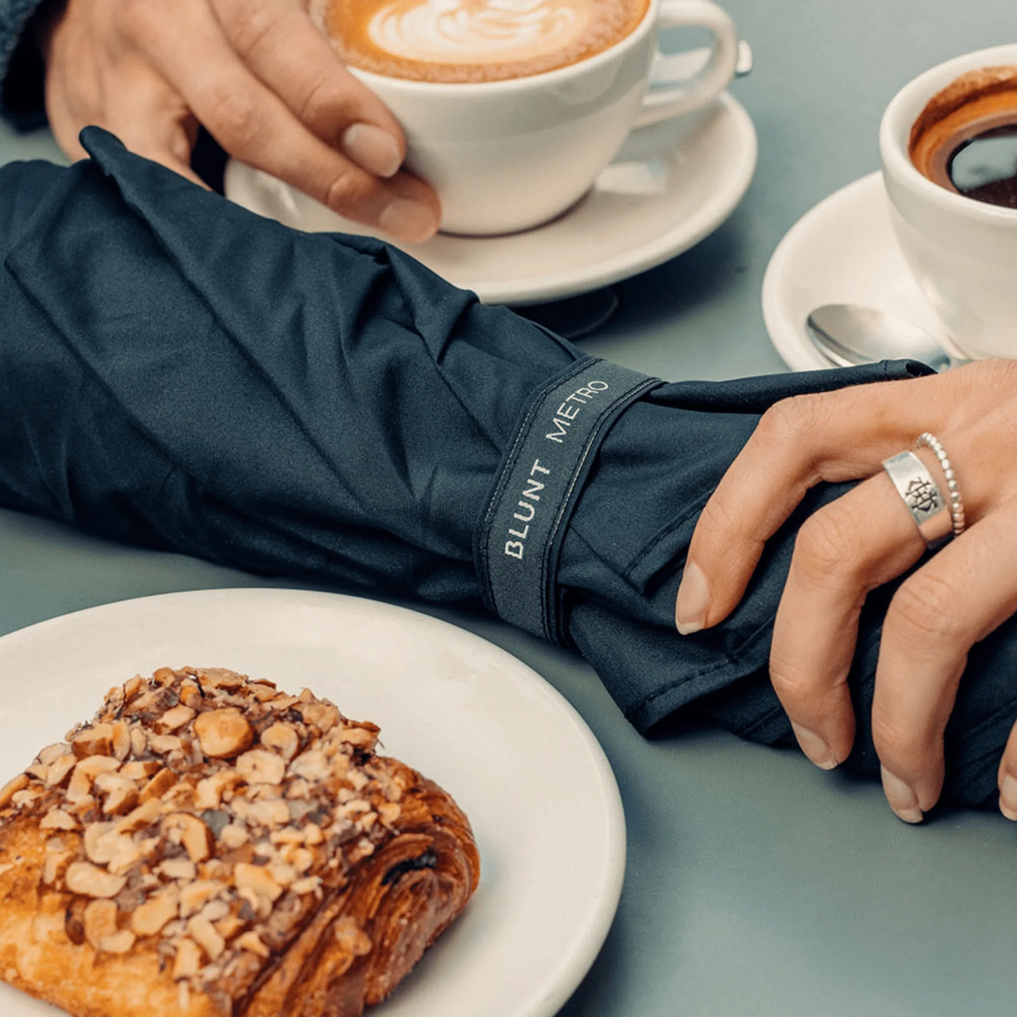 Retracted on a table, the Blunt Umbrella Metro Midnight Navy, which is compact, collapsible and convenient, consisting of the detachable UV fabric canopy, sturdy frame, shaft and handle. Fits in your handbag, tote or backpack. Built for fast living, those who travel light, and any weather.