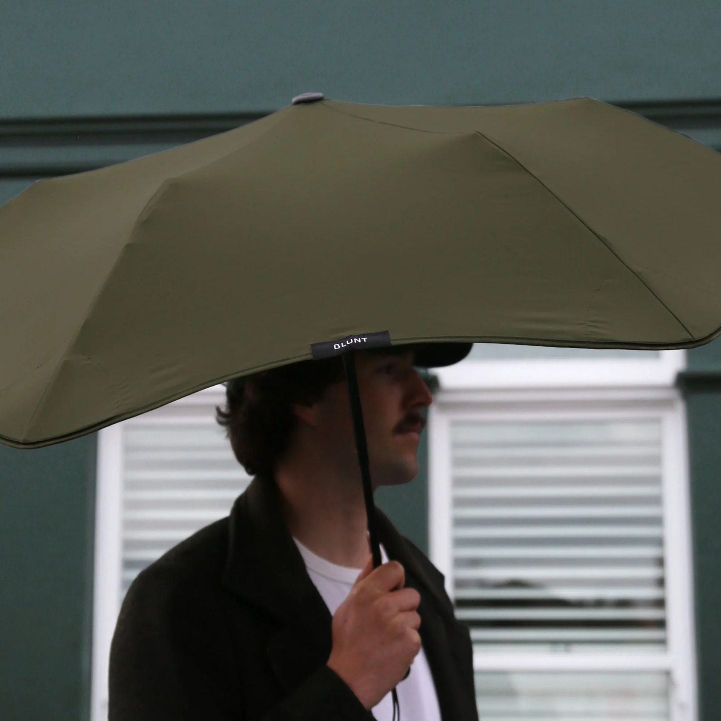 Upclose view of a man using the Blunt Umbrella Metro Moss Green, which a timeless, compact, collapsible and convenient, consisting of the detachable UV fabric canopy, sturdy frame, shaft and handle. Fits in your handbag, tote or backpack. Built for fast living, those who travel light, and any weather.