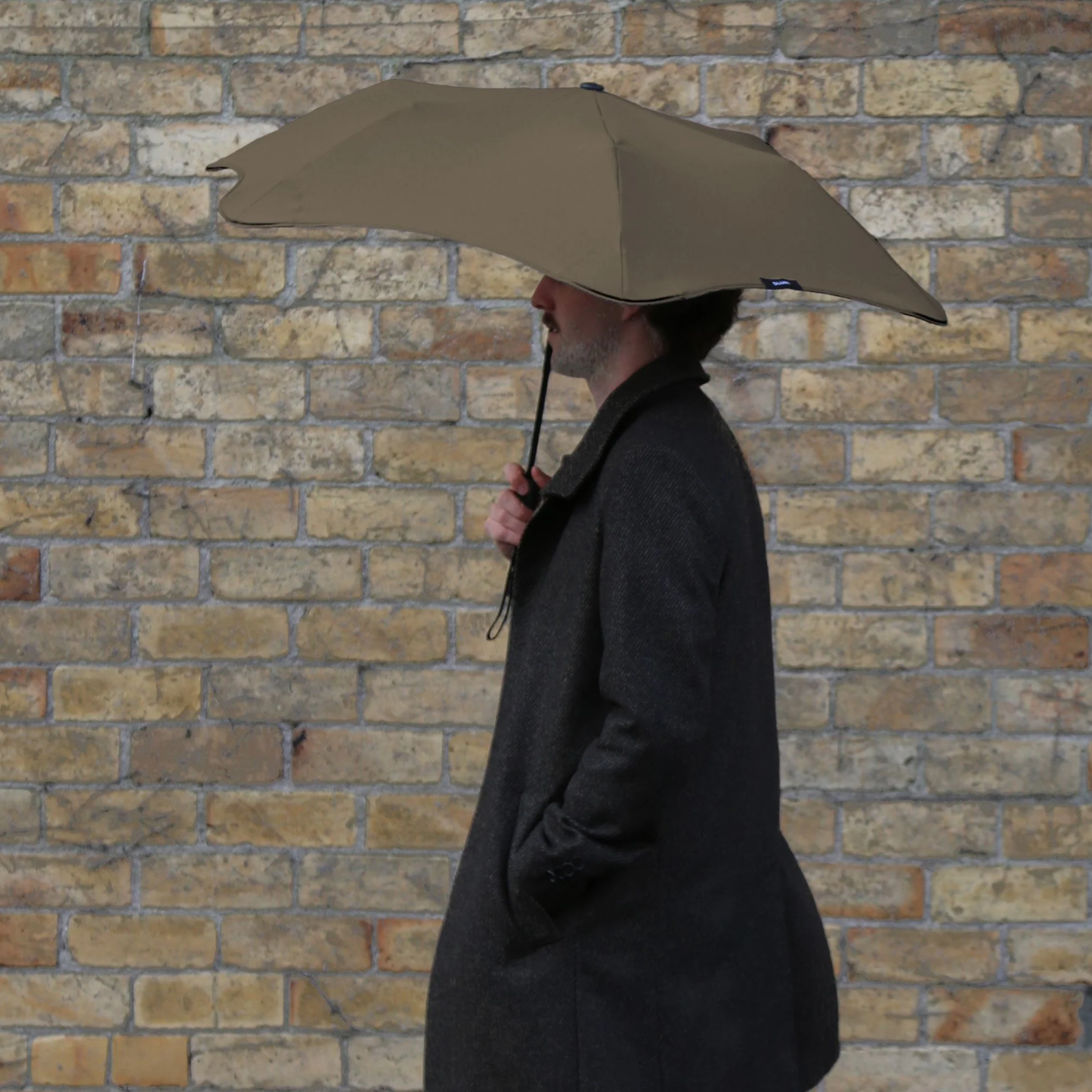 Side view of a man holding the Muted tone Blunt Umbrella Metro Pebble, especially made for those who appreciate understated quality. Compact, collapsible and convenient, consisting of the detachable UV fabric canopy, sturdy frame, shaft and handle. Fits in your handbag, tote or backpack. Built for fast living, those who travel light, and any weather.