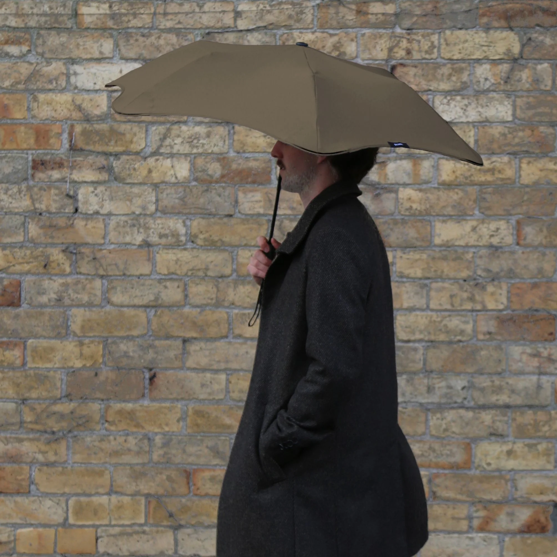Side view of a man holding the Muted tone Blunt Umbrella Metro Pebble, especially made for those who appreciate understated quality. Compact, collapsible and convenient, consisting of the detachable UV fabric canopy, sturdy frame, shaft and handle. Fits in your handbag, tote or backpack. Built for fast living, those who travel light, and any weather.