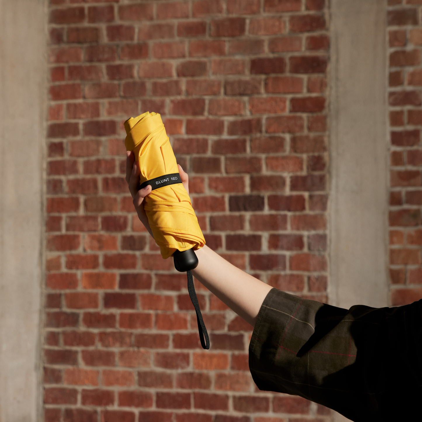 Folded Blunt Umbrella Neo Citrus Yellow, featuring a compact design with high tensioned canopy, wind tested construction and recycled rPET fabric for rain or shine.