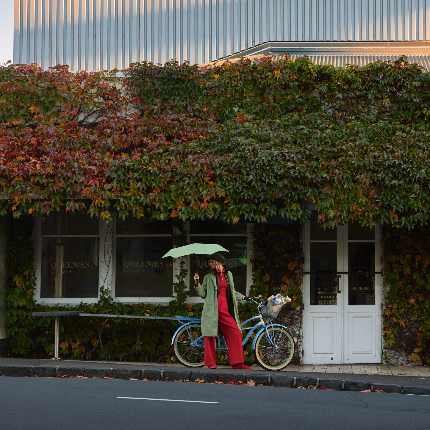 A woman parking her bicycle holding the open Blunt Umbrella Sage Green at 98cm, featuring a compact design with high tensioned canopy, wind tested construction and recycled rPET fabric for rain or shine.