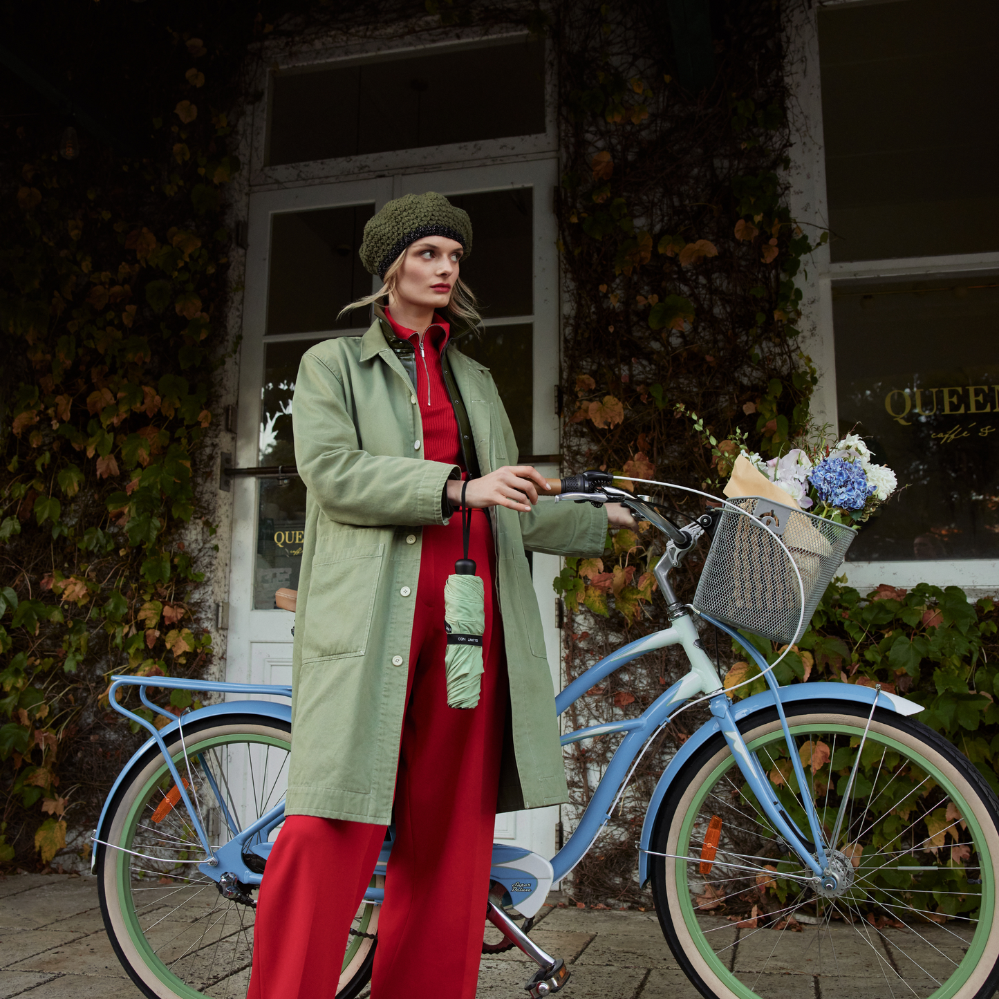 A woman with the Blunt Umbrella Sage Green hanging at her hand that features a compact design with high tensioned canopy, wind tested construction and recycled rPET fabric for rain or shine.