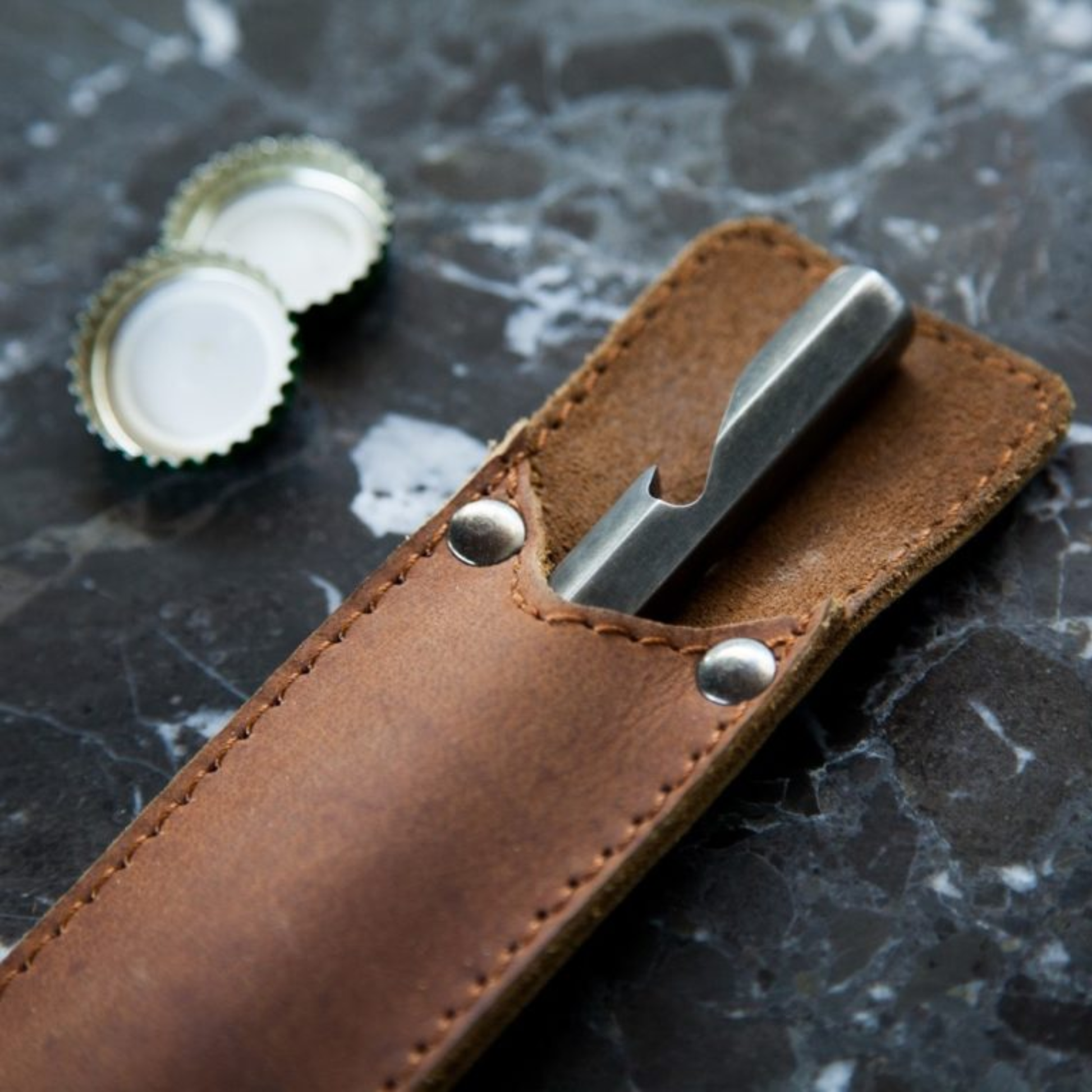 Close up of Brut Homeware burnt stainless steel bottle opener with custom buffalo leather sleeve, handcrafted in India, heavyweight 230g design for durable and stylish use, ideal as a luxury or barware gift.