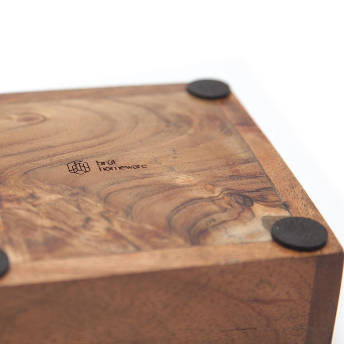 Close-up of the corner of the Brut Coffee Knock Box, highlighting its visible wood grain patterns, four black round pads on the bottom, and the engraved Brut logo.