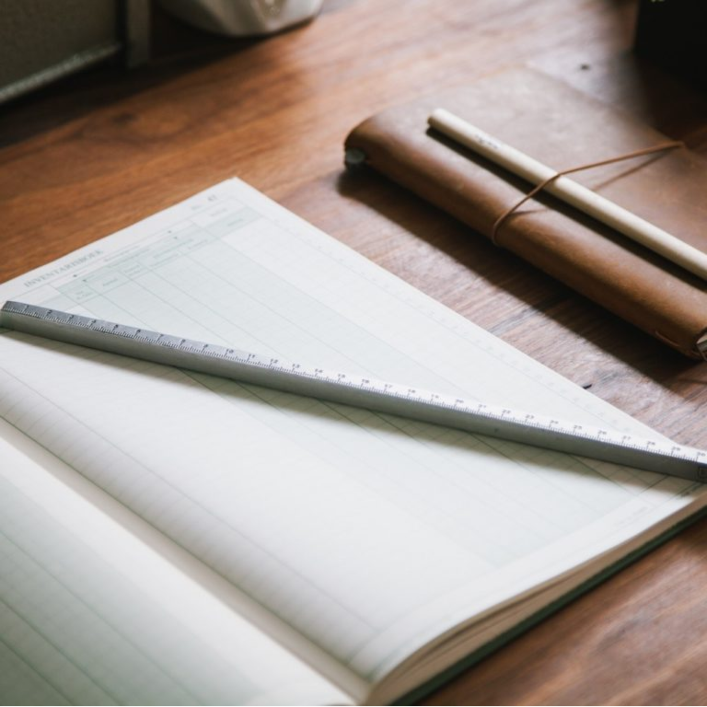 Shown with a notebook Brut Homeware aluminium measuring rod featuring dual metric and imperial scales, 30 cm / 12 in long, lightweight and precision-made, packaged in a black carton-ideal for designers, artists, and stationery lovers seeking a sleek, durable tool.