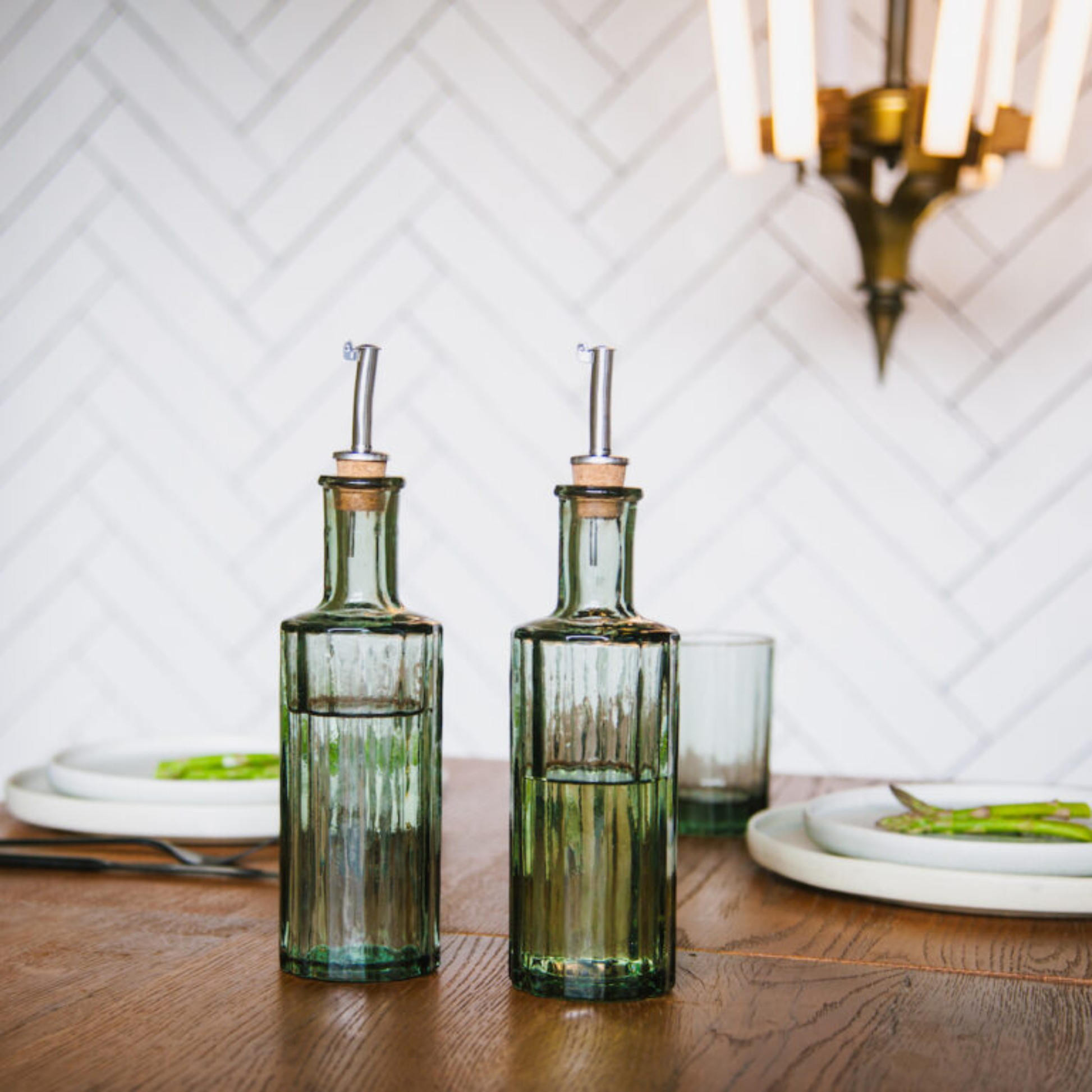 Shown on the table Brut Homeware Art Deco-inspired oil and vinegar bottles, mouth-blown from recycled glass with natural cork pourers and anti-drip caps - elegant, sustainable, and handmade in India.