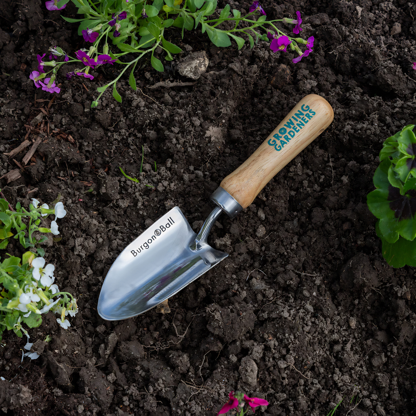 Burgon & Ball Kids Hand Trowel Stainless Steel and hardwood handle with strong hanging cord, seen on the soil with the handle up.