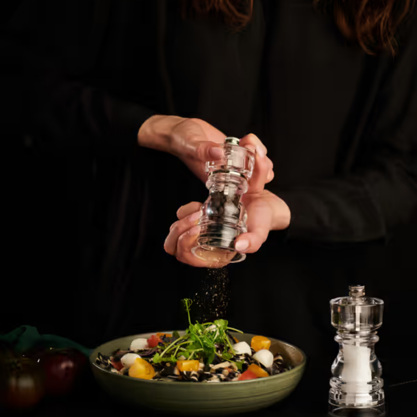 Woman using pepper mill from Cole & Mason London salt and pepper mills set, 13cm, made from clear durable acrylic with ceramic and Precision+ carbon steel mechanisms, classic yet contemporary design with lifetime guarantee.