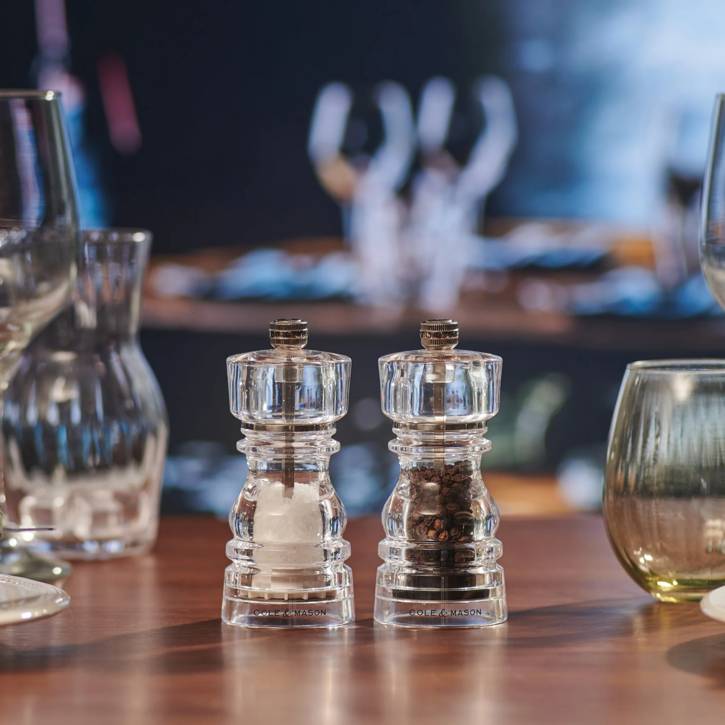 Table view of Cole & Mason London salt and pepper mills set, 13cm, made from clear durable acrylic with ceramic and Precision+ carbon steel mechanisms, classic yet contemporary design with lifetime guarantee.